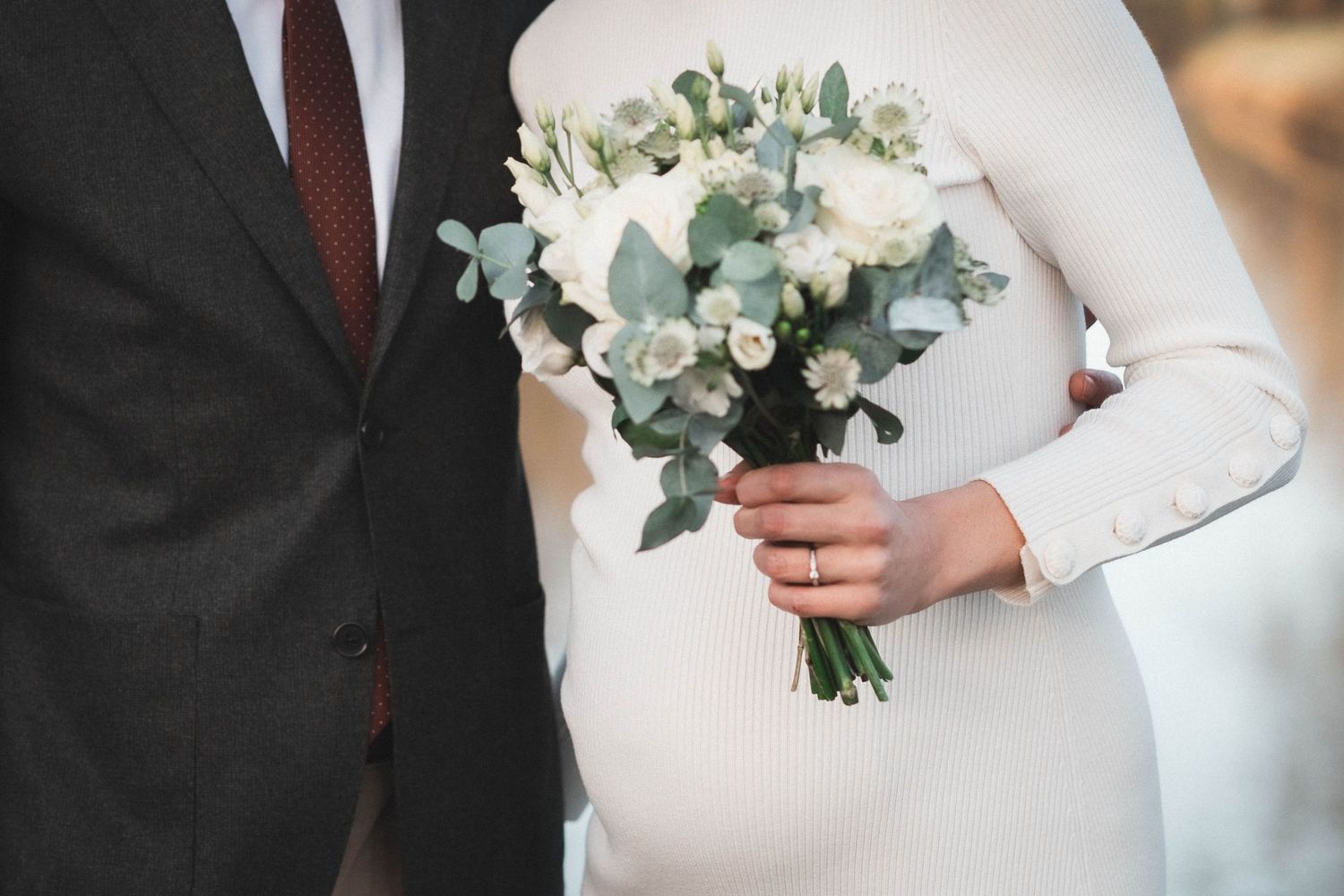 A white wedding bouquet with delicate greenery and flowers held against formal attire.
Mariée enceinte tenant son bouquet tenant son mari.