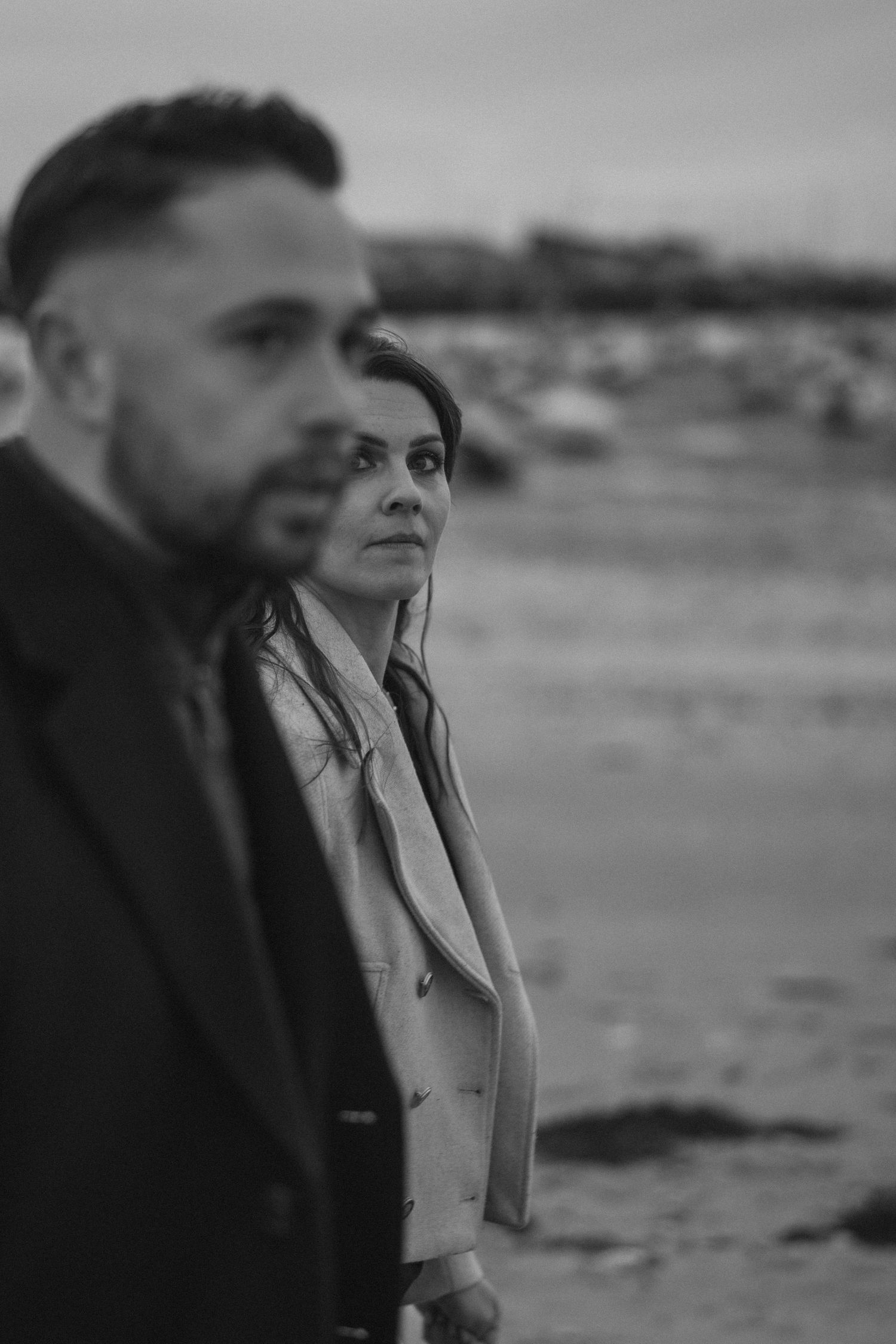 A moody black and white photograph of a couple on an overcast beach.
Couple en noir et blanc marchant sur la plage.