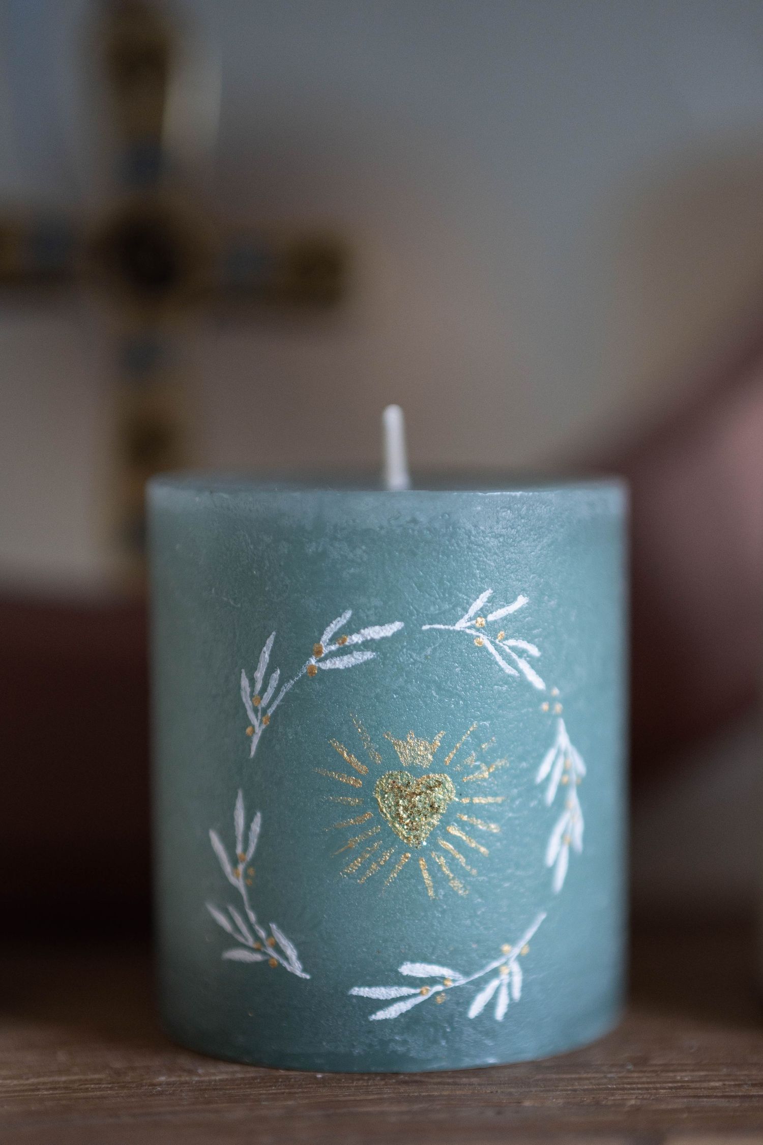 Decorative green pillar candle featuring hand-drawn botanical design with gold sun detail.
Bougie bleue avec coeur sacré peint dessus.