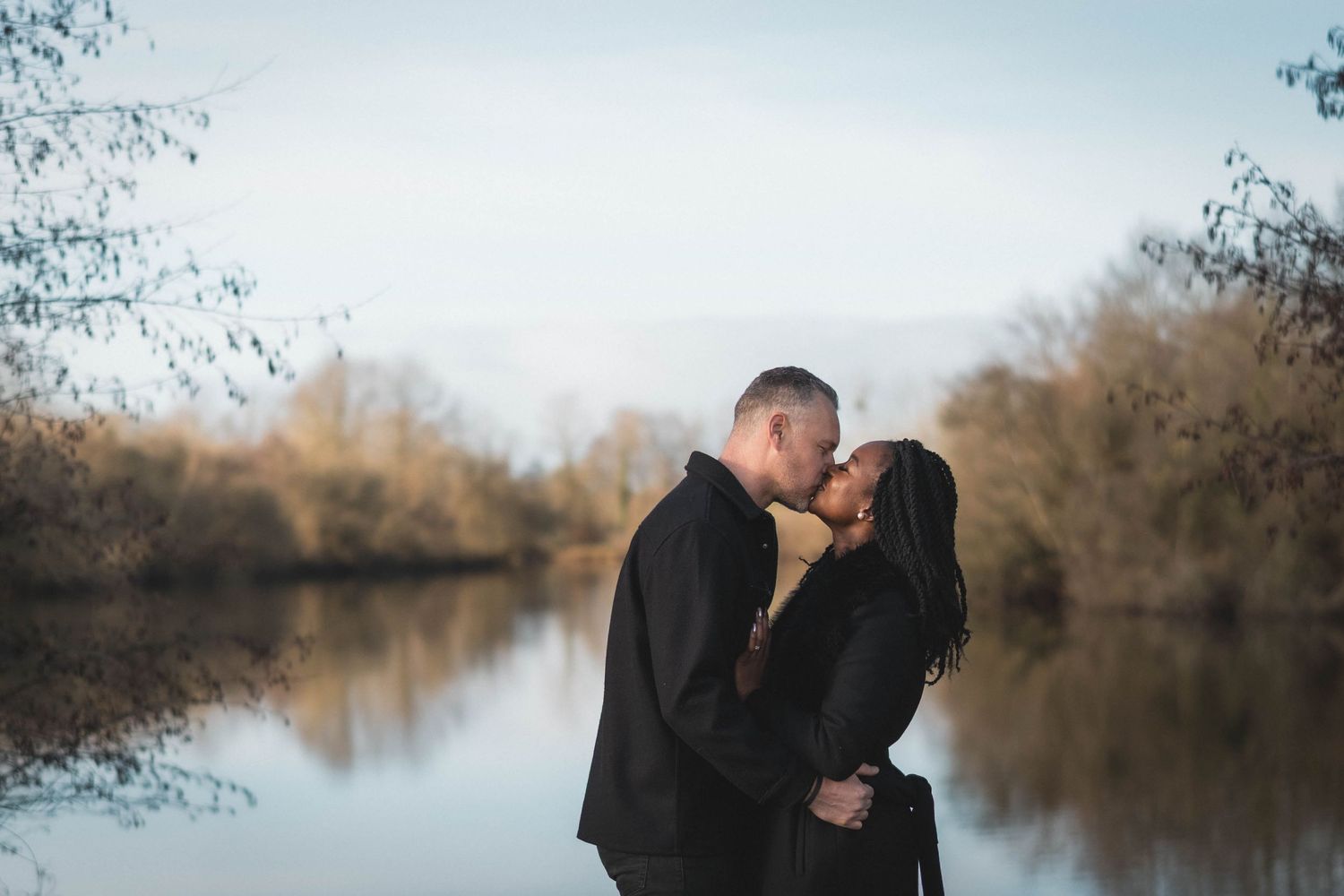 A romantic couple shares an intimate moment by a serene lake during golden hour.
Couple s'embrassant au bord d'un étang.