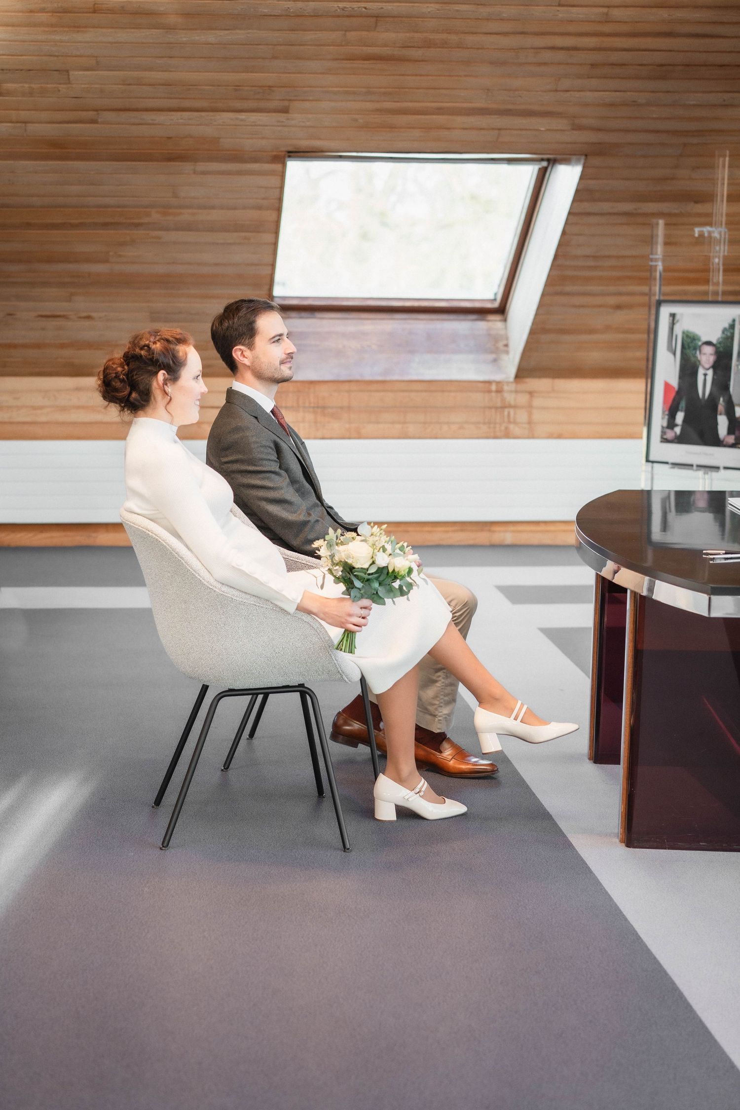 Modern interior with wooden ceiling and grey chair where a couple reviews paperwork.
Mariés assis durant la cérémonie civile.