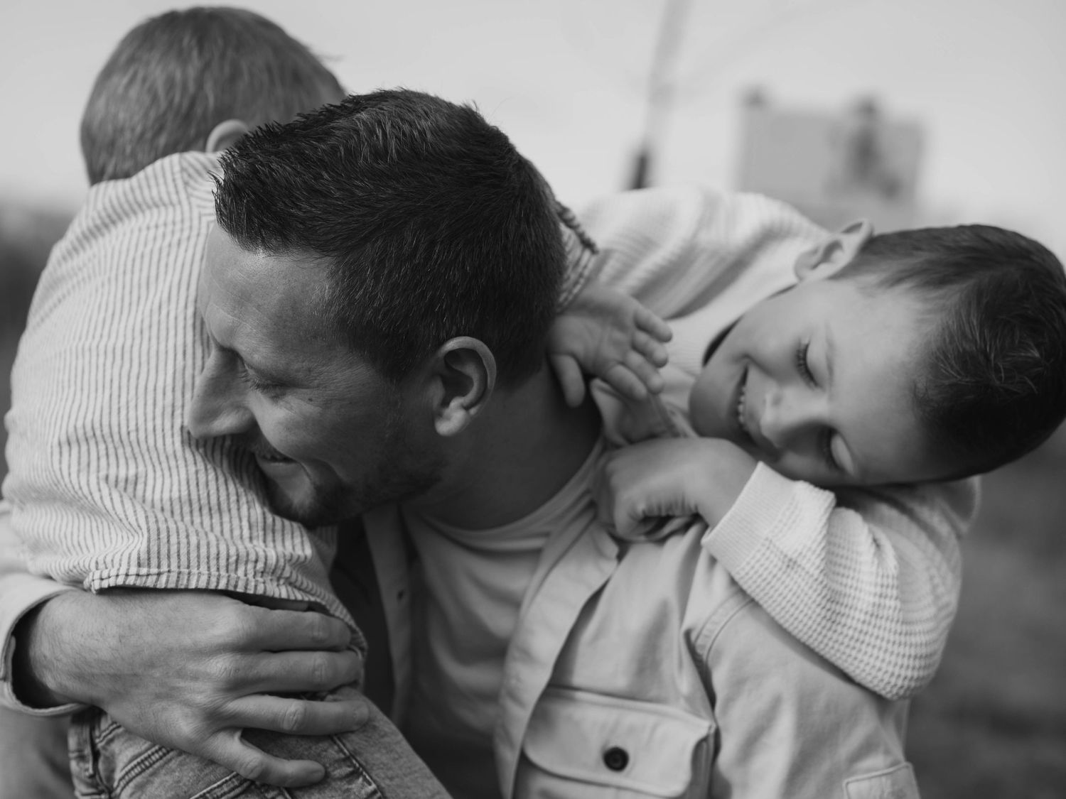 Series of intimate black and white photographs showing tender moments of connection.
Un père et ses deux fils jouant et se câlinant