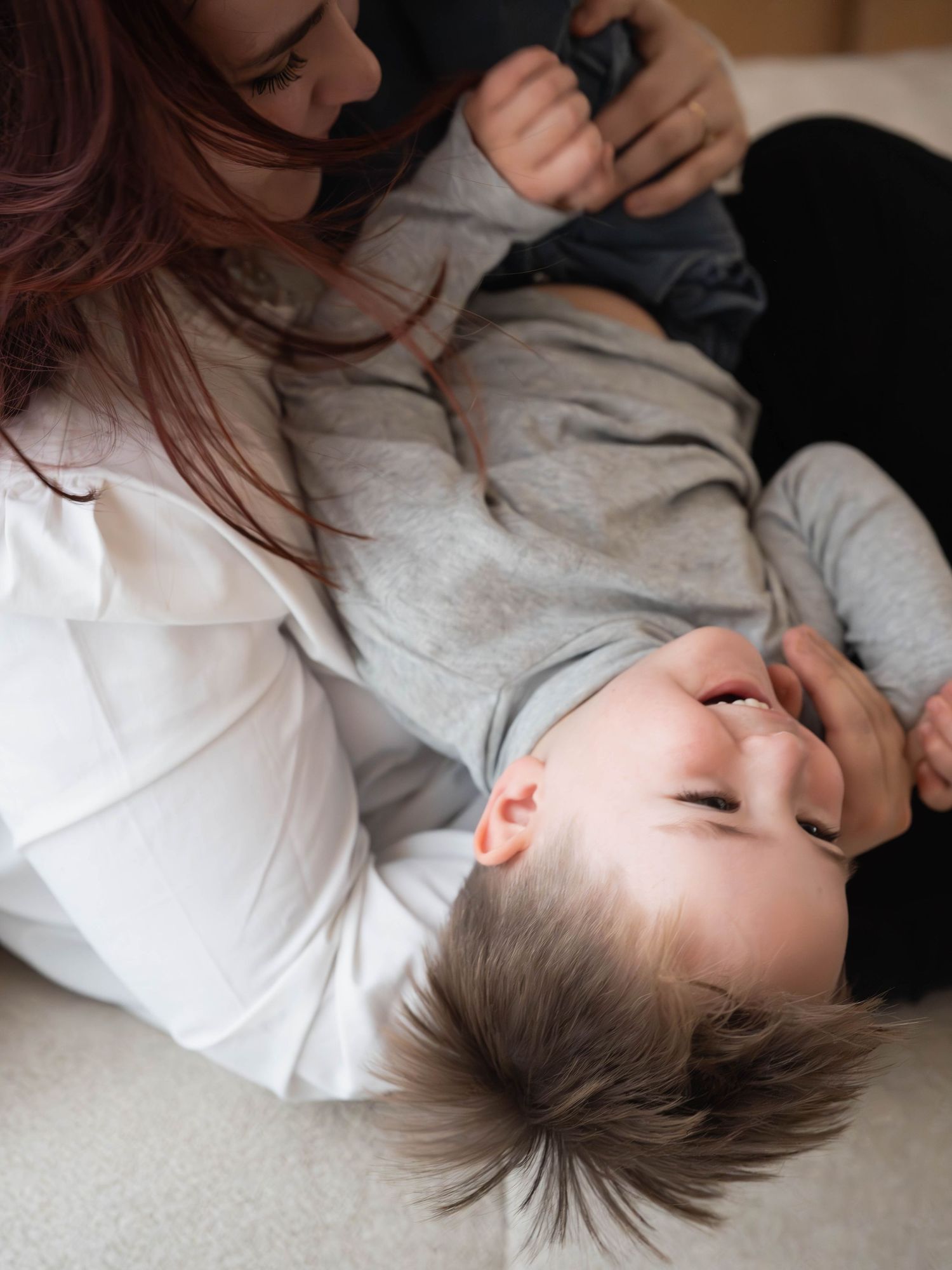Intimate moment of parent and child playing together on bed.
Moment de câlin et jeu entre une mère et son fils.
