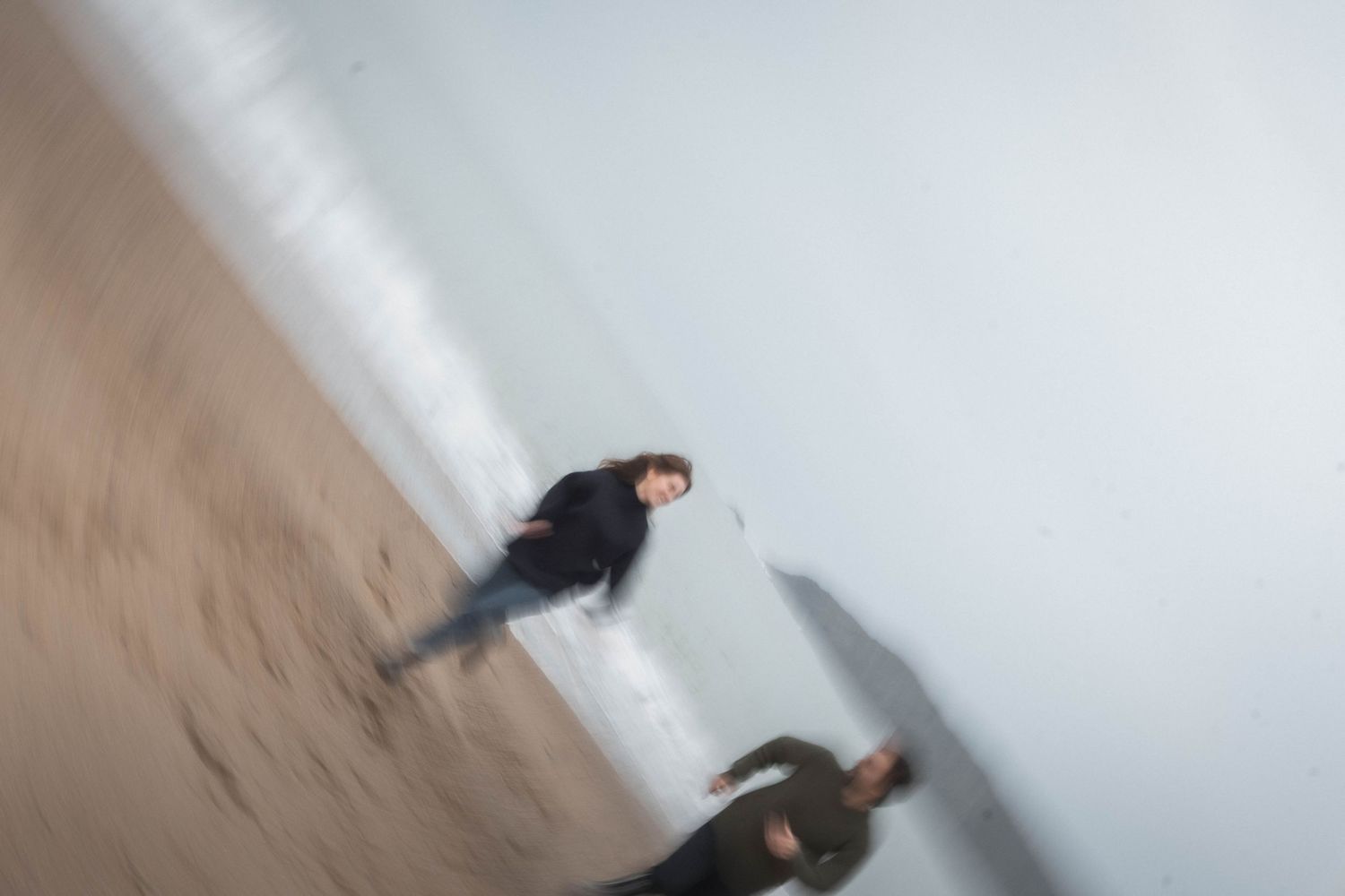 Motion blur of figures walking along a white interior wall.