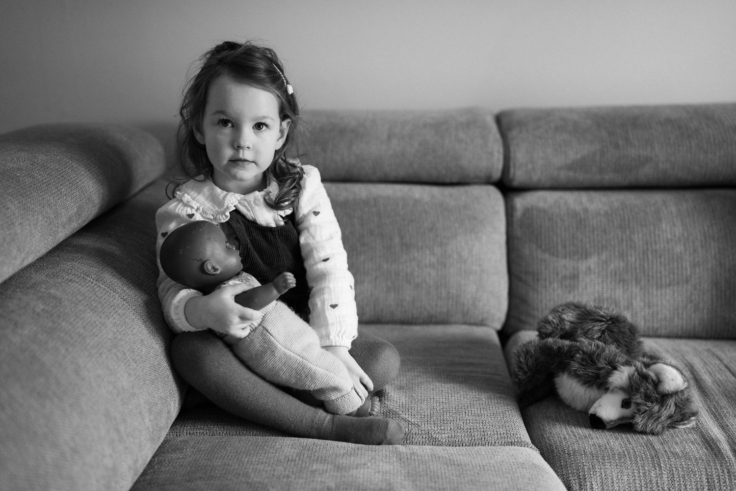 Black and white photographs showing quiet moments on a grey couch.
Petite fille avec sa poupée et son doudou sur canapé en noir et blanc.