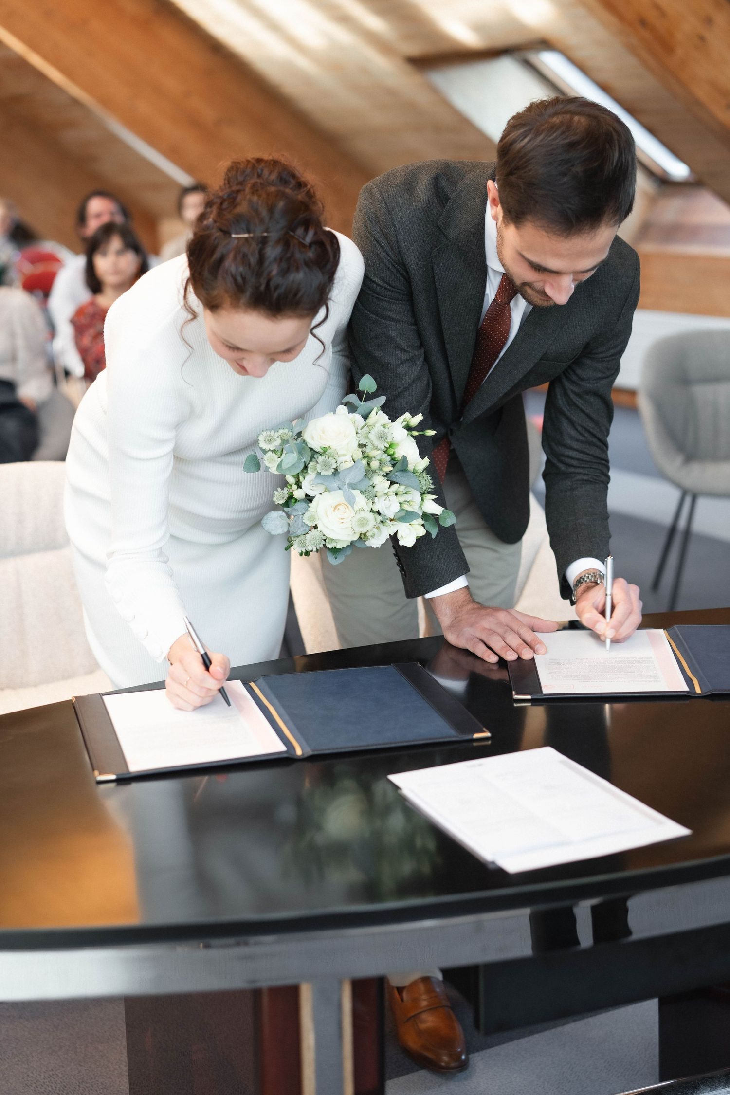 A couple signing official documents at a modern desk with white flowers.
Mariés signant les registres durant la cérémonie civile.
