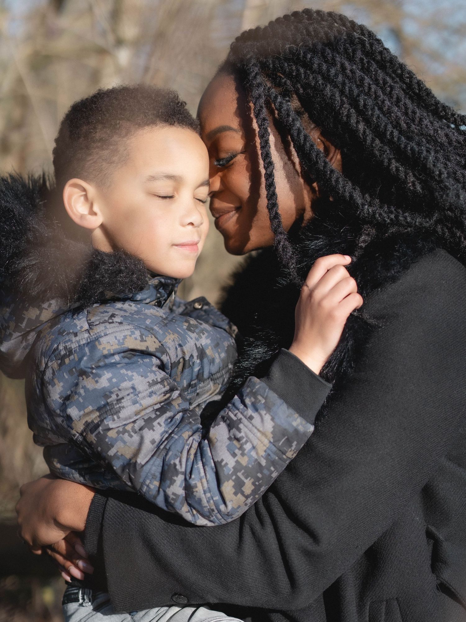 Two people sharing an intimate embrace outdoors with winter trees in the background.
Câlin entre une mère et son fils dans la nature.
