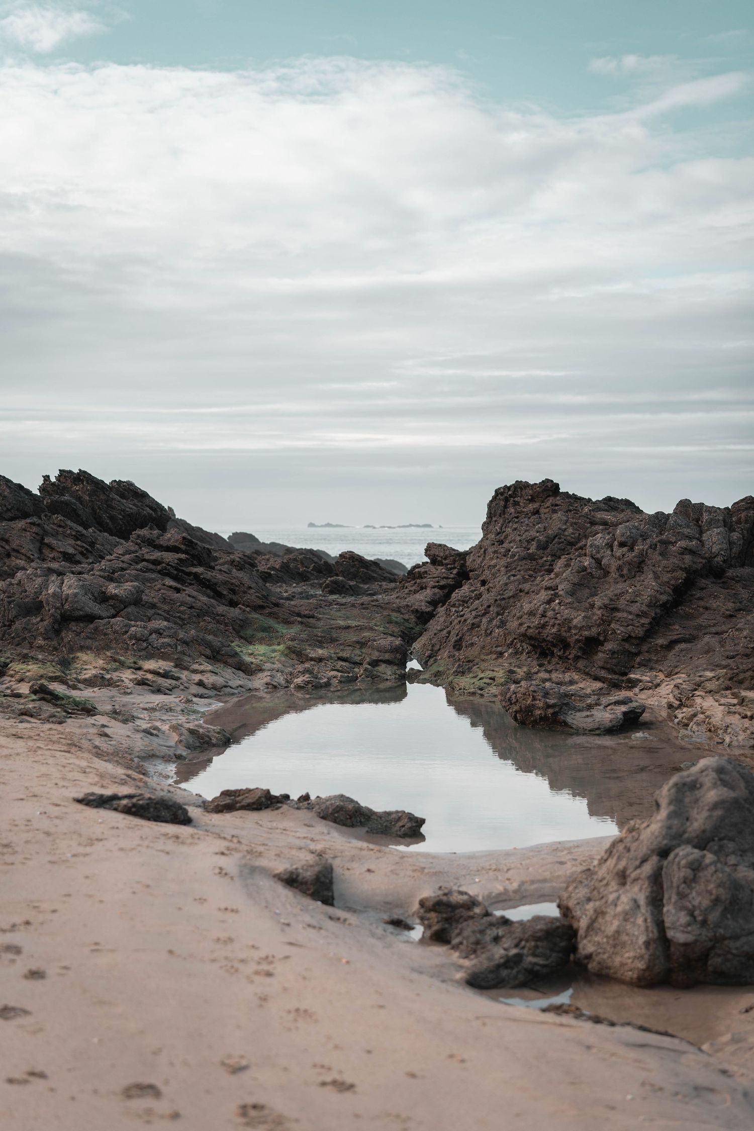 Rocky coastal tide pools with calm water reflecting cloudy skies.
Rochers et ciels au bord de la mer. Flaque reflétant les nuages.