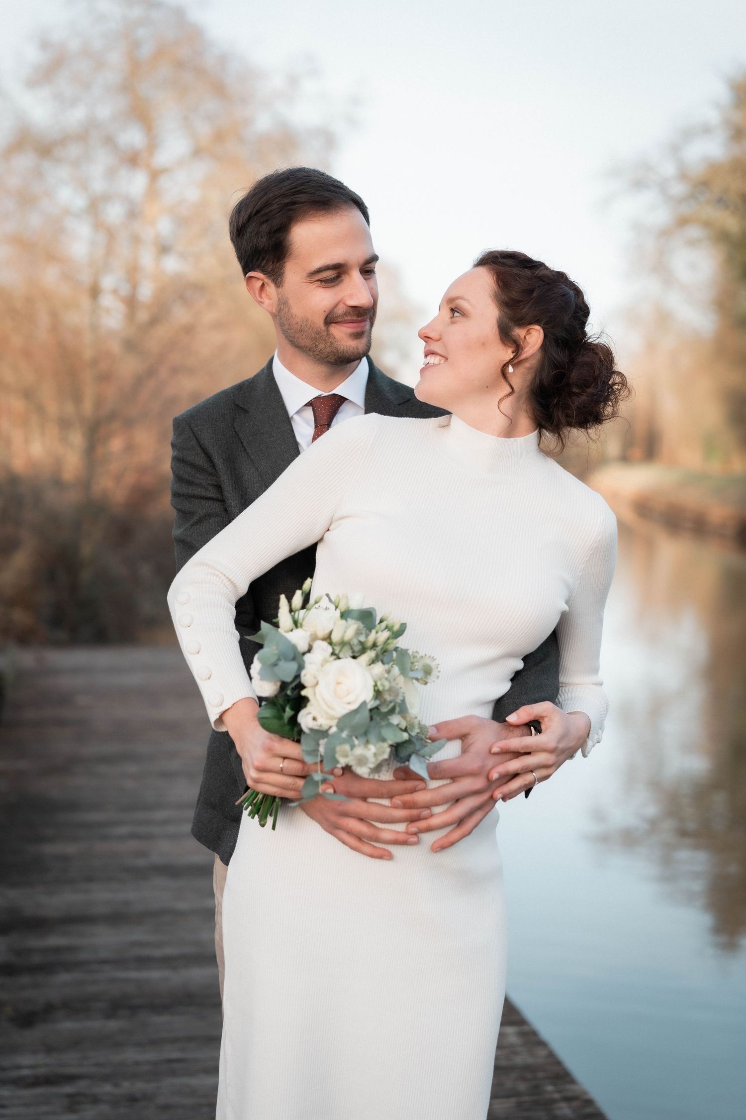 Couple sharing intimate moment by lake with white floral bouquet.
Couple de mariés avec femme enceinte et son bouquet s'enlaçant.