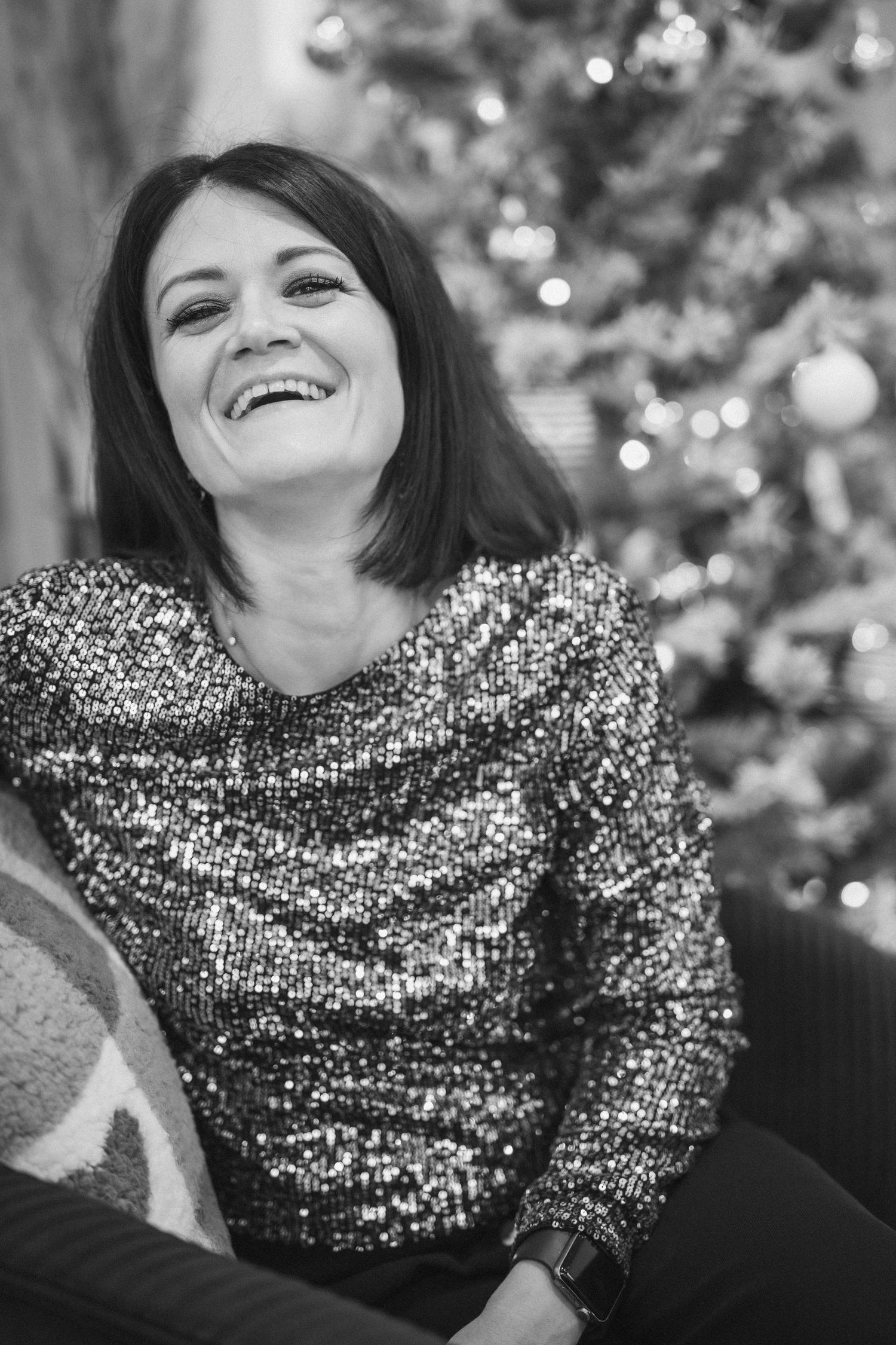 Festive holiday portrait with sparkly sequined top and Christmas tree in background.
Portrait en noir et blanc d'une femme riant.