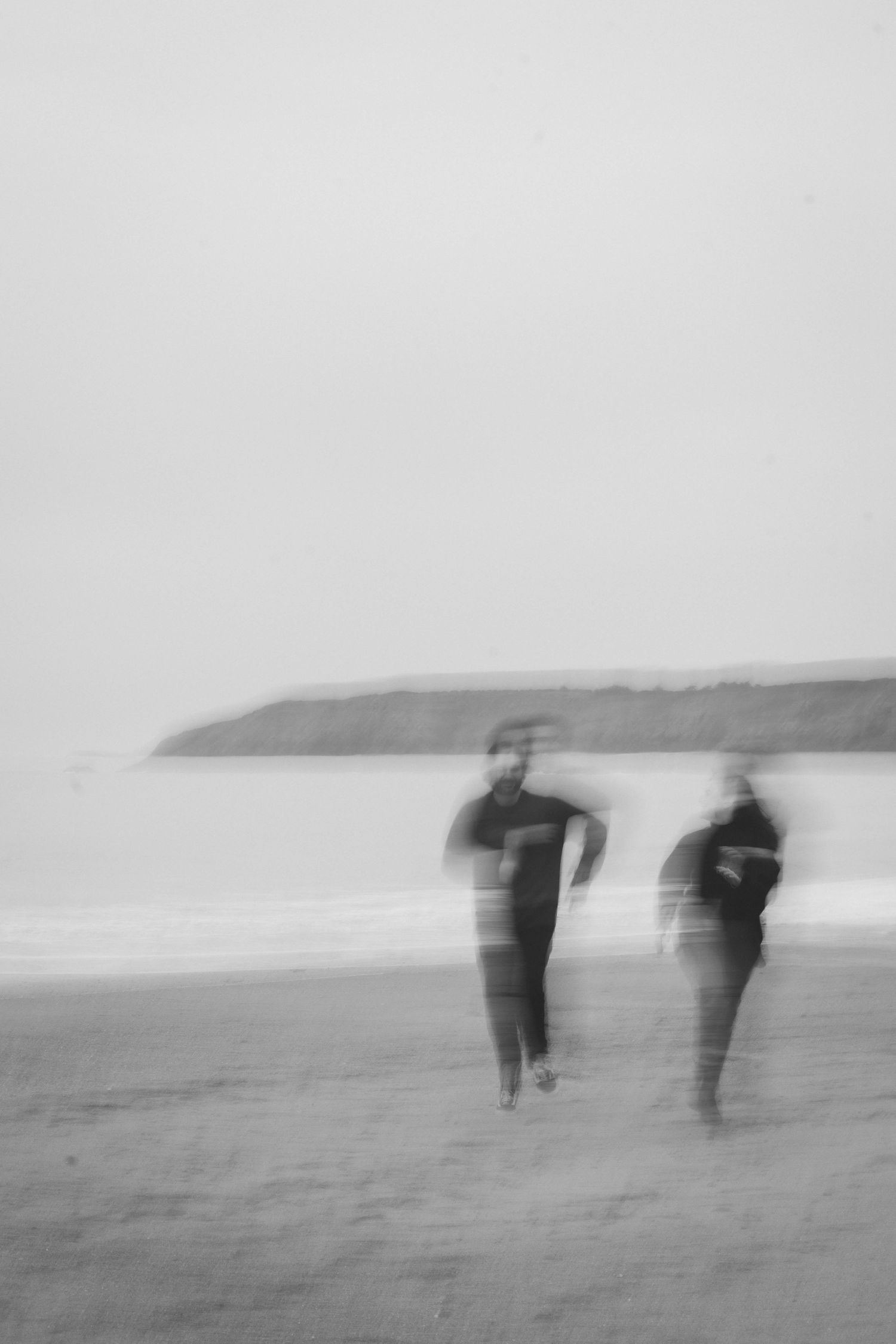 Blurred black and white photograph of figures walking on a misty beach.
Photo artistique floue d'un couple courant sur la plage.
