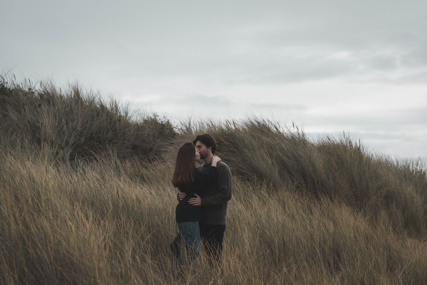 A couple embraces in tall grass on a hillside overlooking the ocean.
Couple s'embrassant dans les hautes herbes.