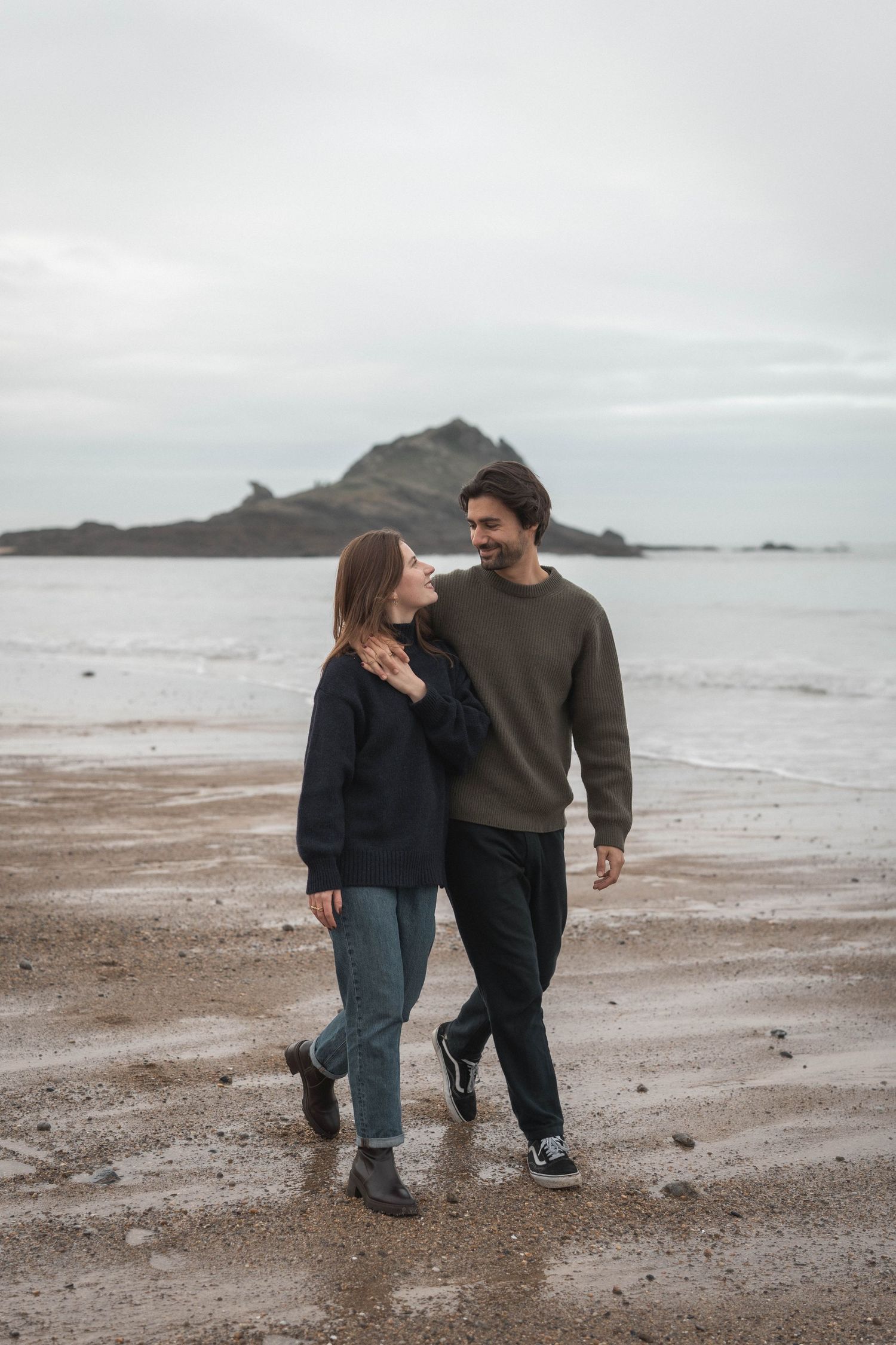 Casual couple walking on beach with rocky coastline in background.
Couple marchant sur la plage se tenant la main