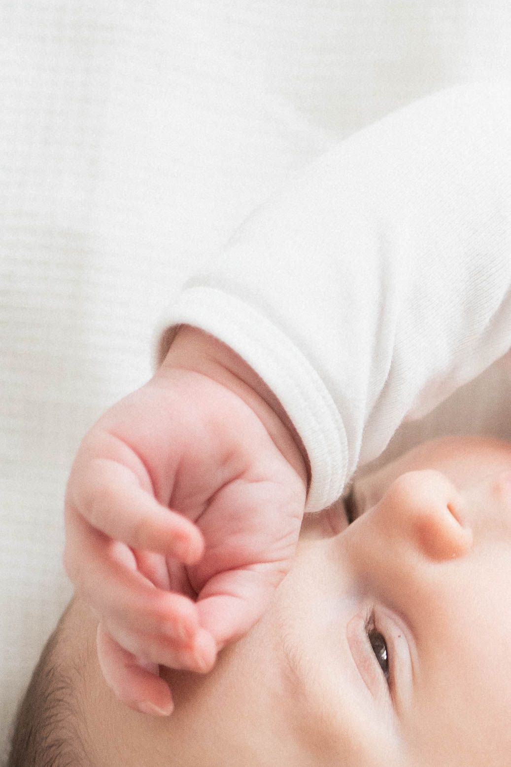 Soft close-up portrait of a sleeping baby's face against white fabric.
Main et haut du visage d'un bébé.