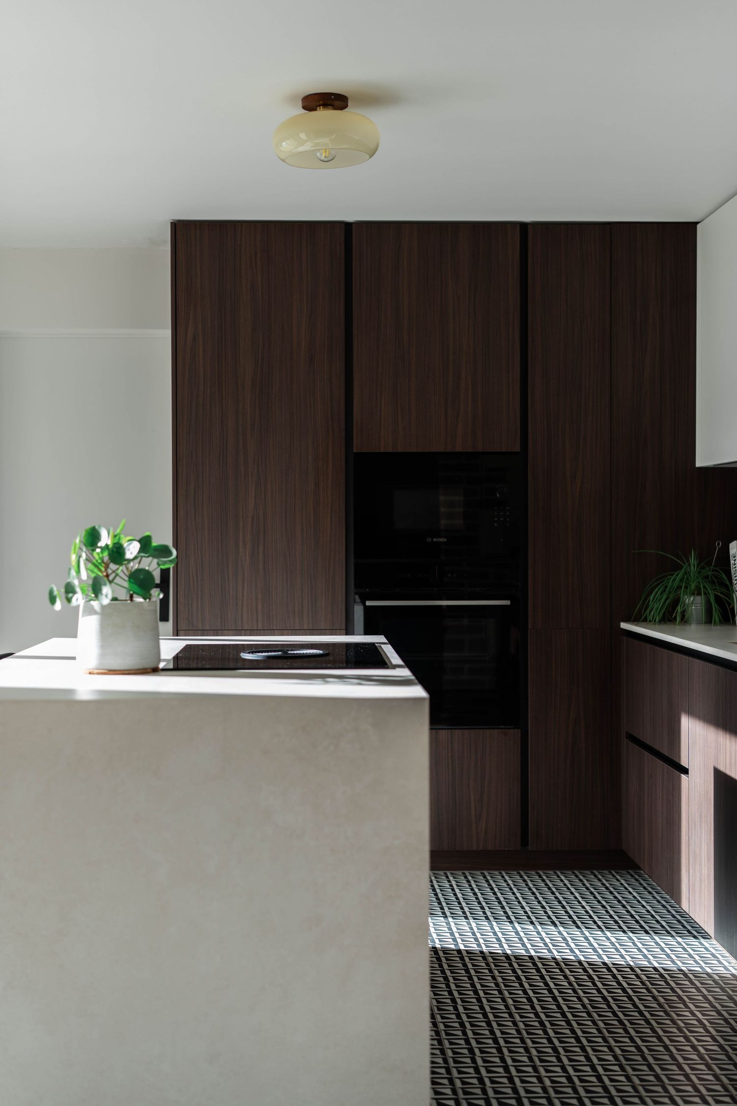 Modern minimalist kitchen with dark wood cabinets, white counters, and geometric patterned flooring.
cuisine contemporaine et moderne.
