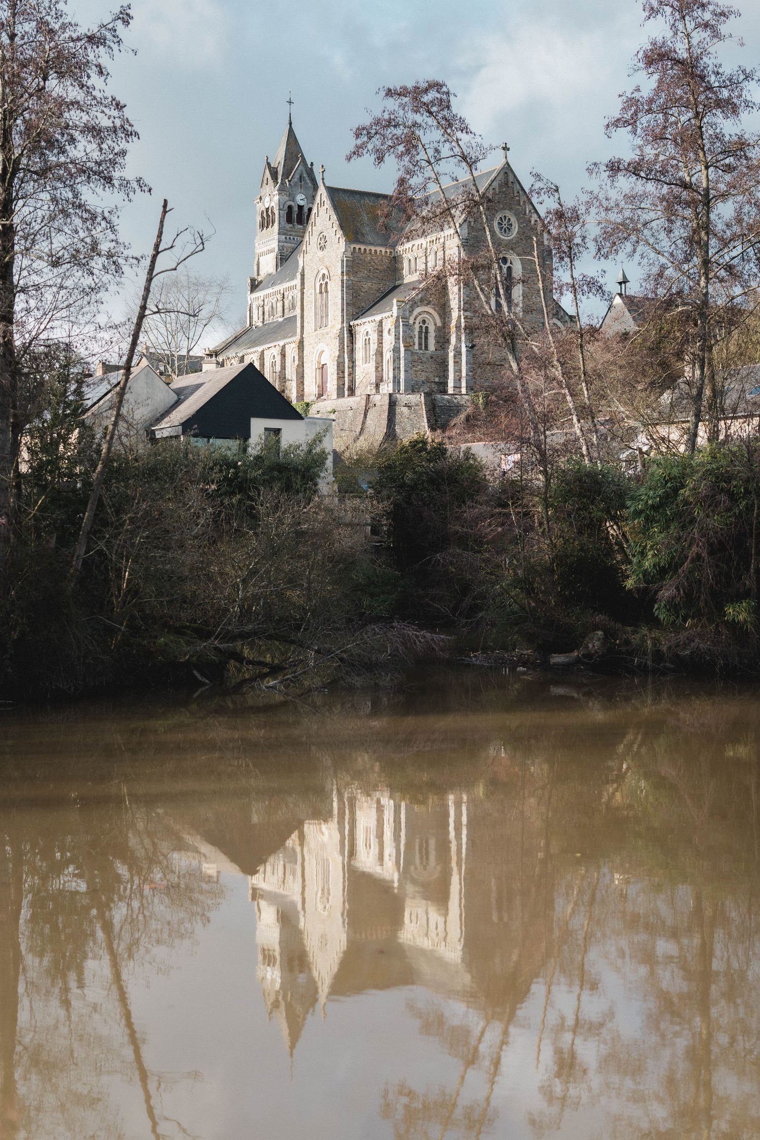 Historic church buildings reflected in calm brown waters with autumn trees along the shoreline.
église et son reflet dans un étang.