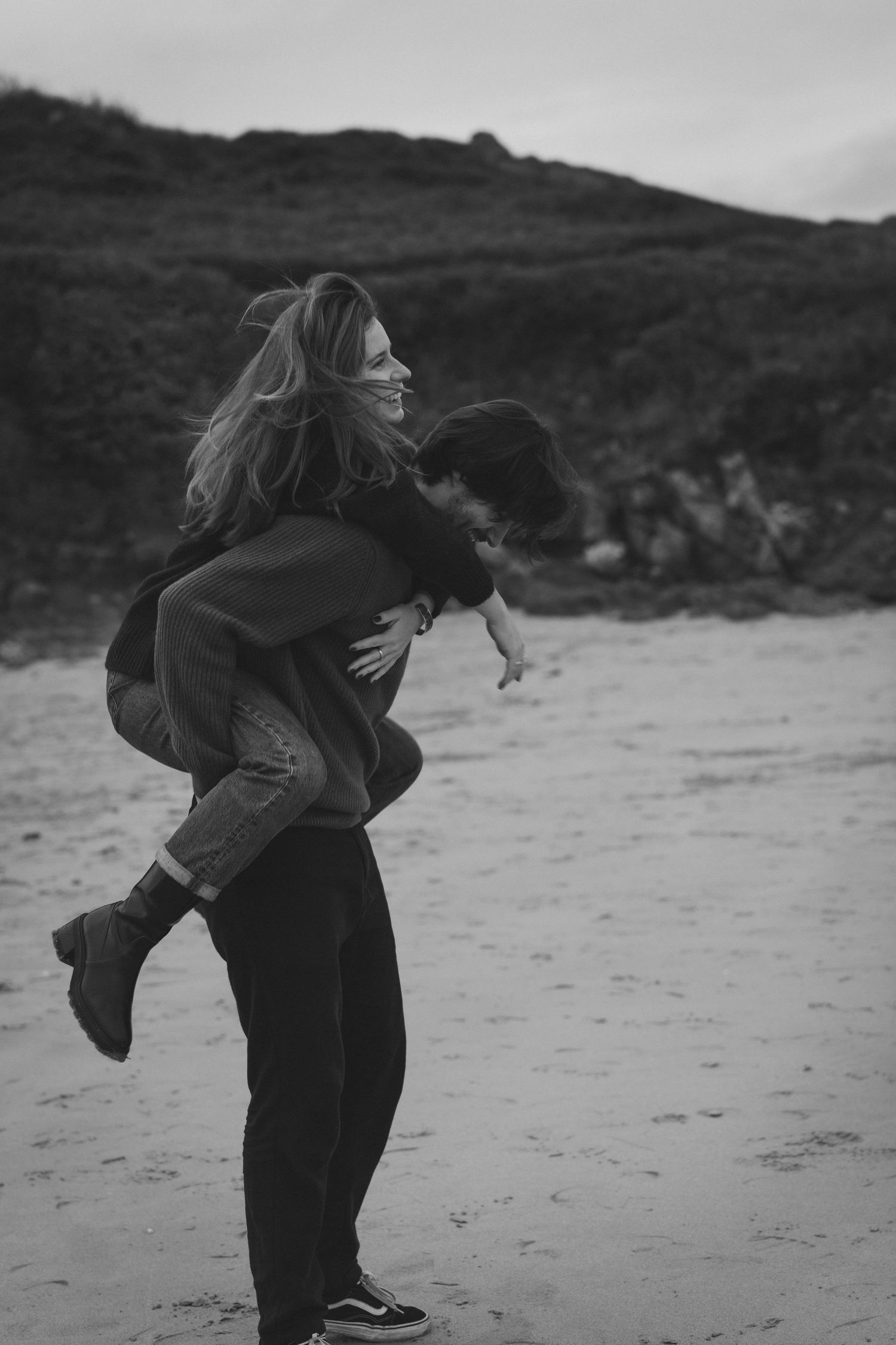 Black and white beach photography of playful moments.
Photo en noir et blanc d'un couple qui s'amuse : femme sur le dos de l'homme.