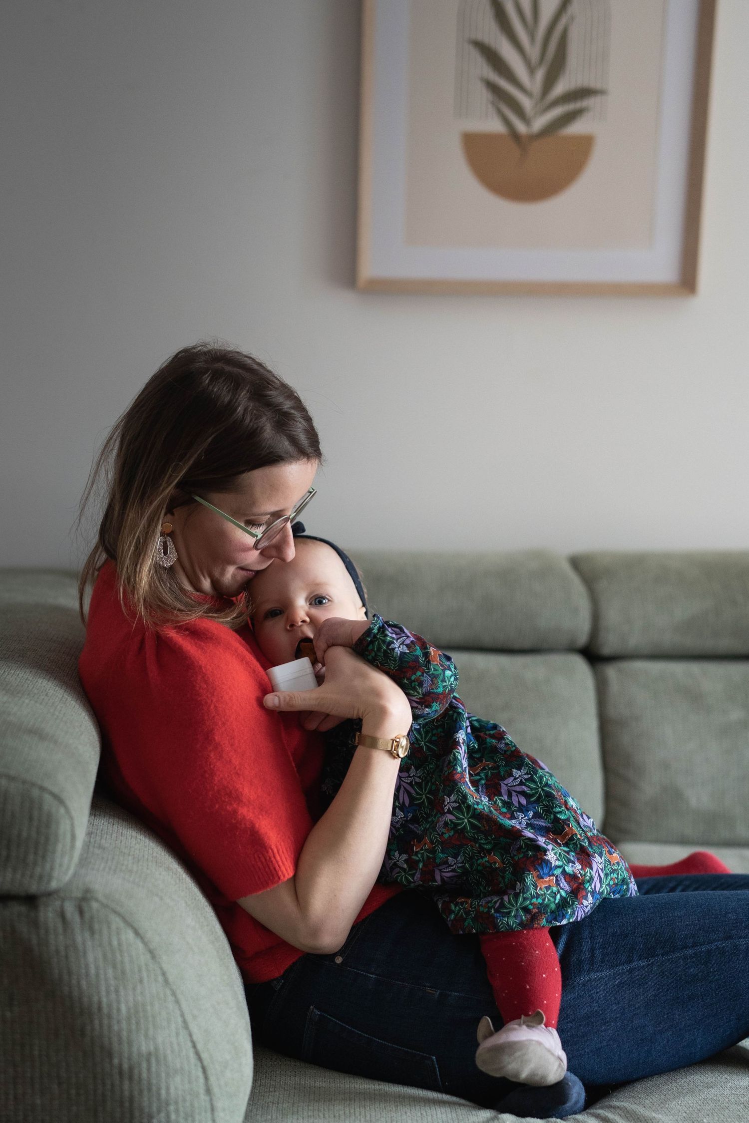 Person in red sweater resting on mint green couch with decorative wall art visible in background.
Câlin d'une mère et son bébé sur canapé.