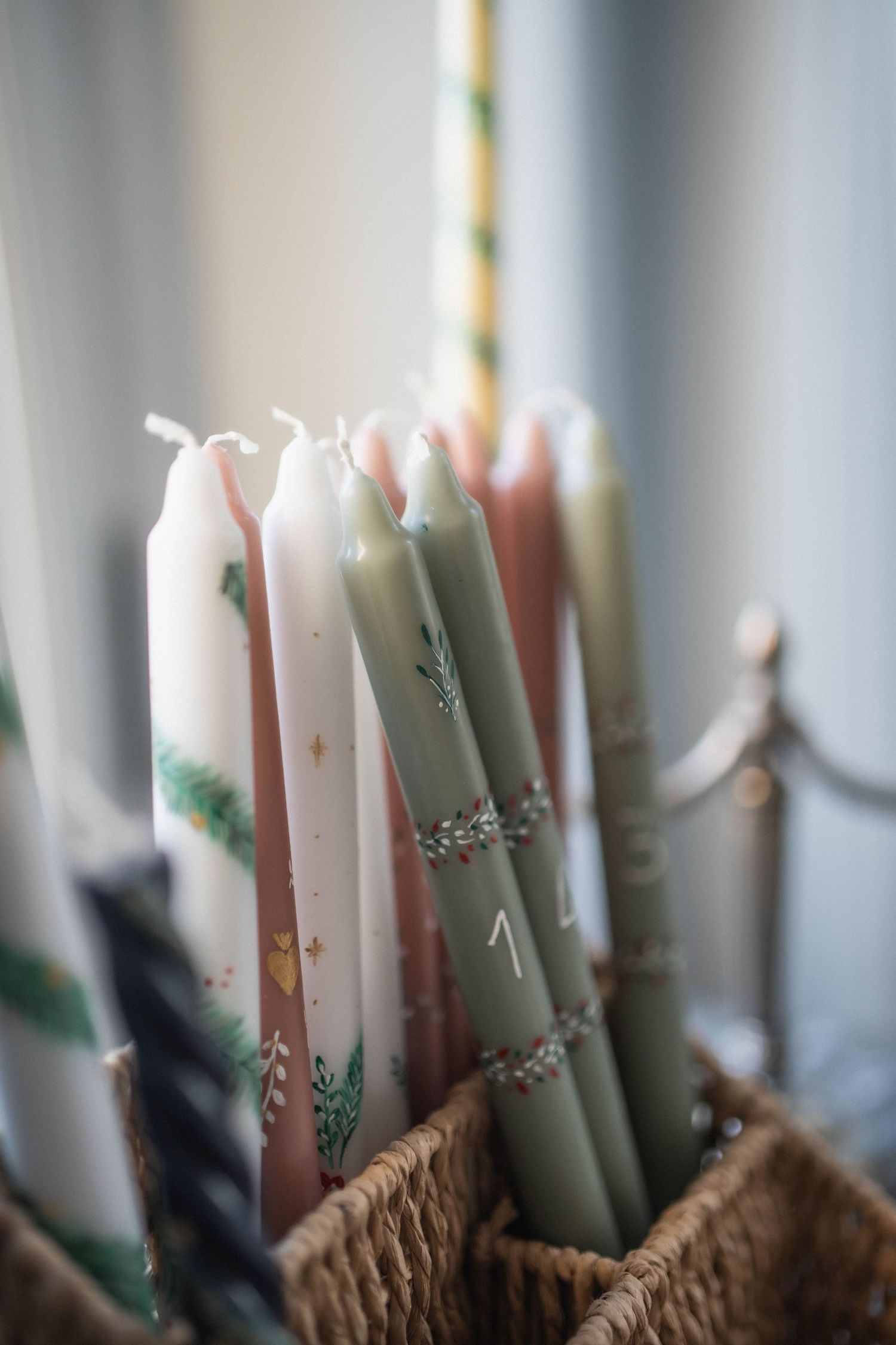 Collection of decorative pastel and sage green candles arranged in a woven basket.
Collection de cierges peints avec symboles chrétiens
