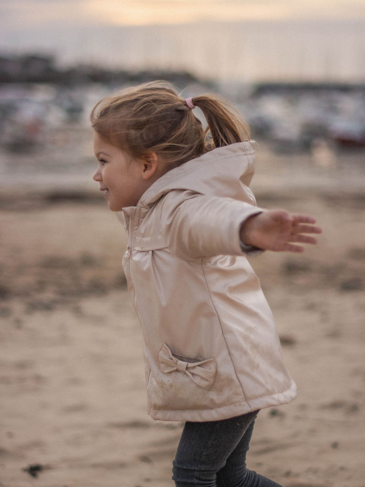 Child running joyfully on a beach with arms spread wide.
Petite fille qui court joyeusement sur la plage, avec les bras en avion.