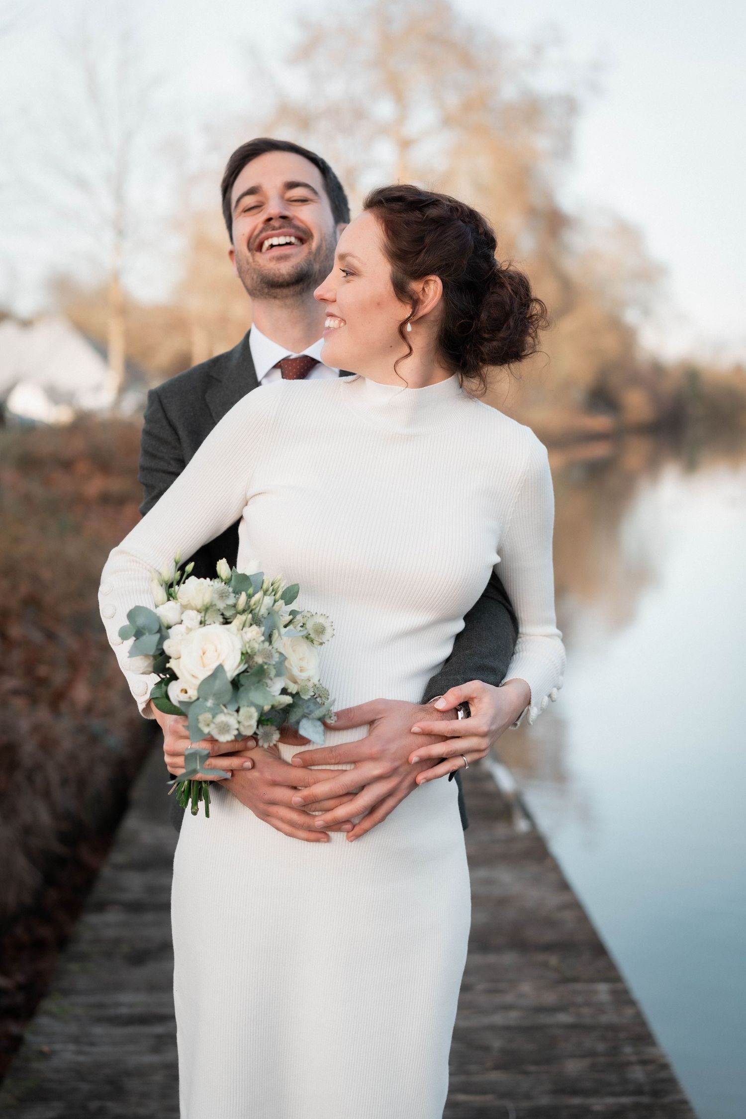Romantic waterfront portrait of a couple embracing with autumn trees in background.
Couple de mariés avec femme enceinte et son bouquet s'en