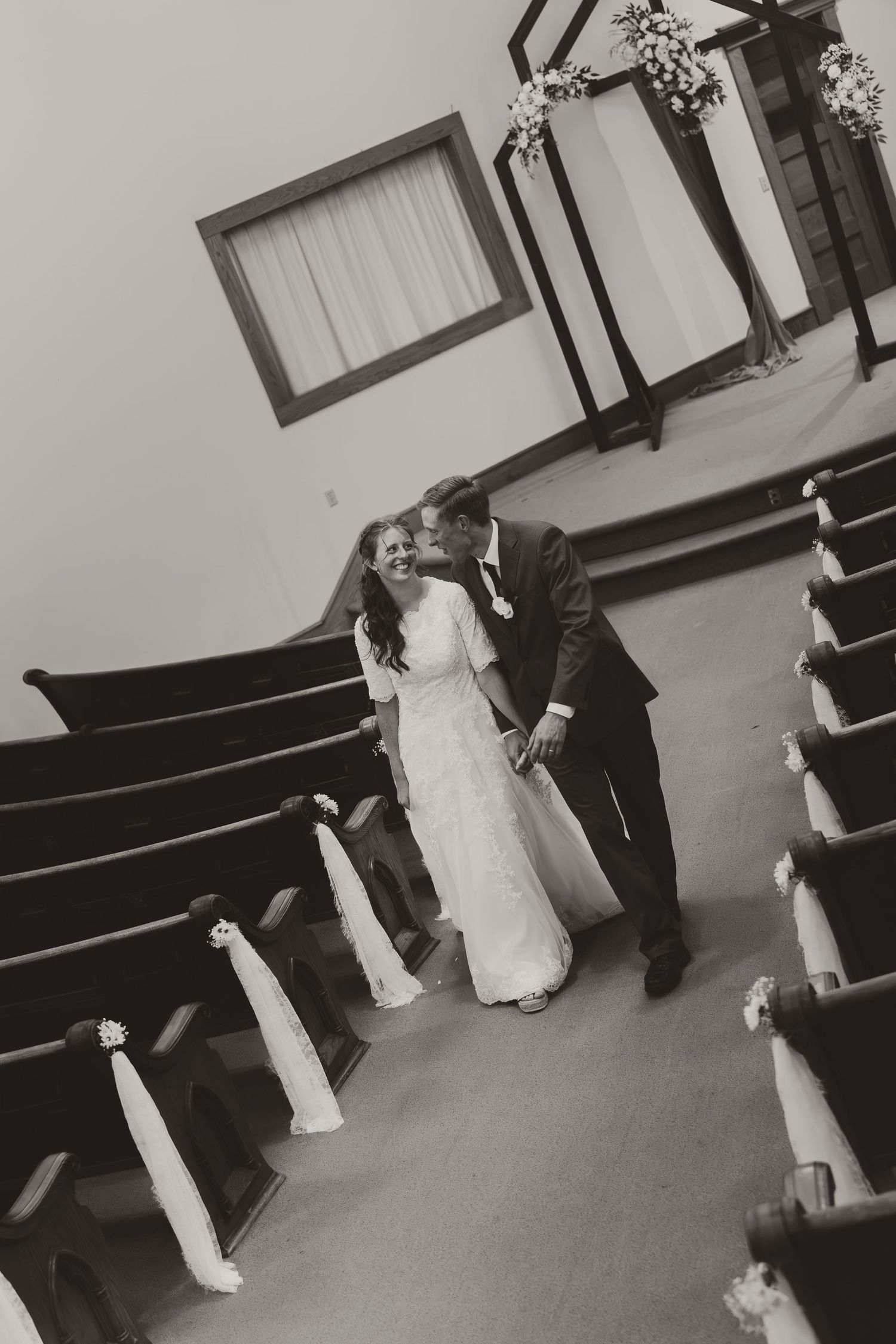Black and white photo of a bride and groom kissing in a church aisle after their wedding ceremony.