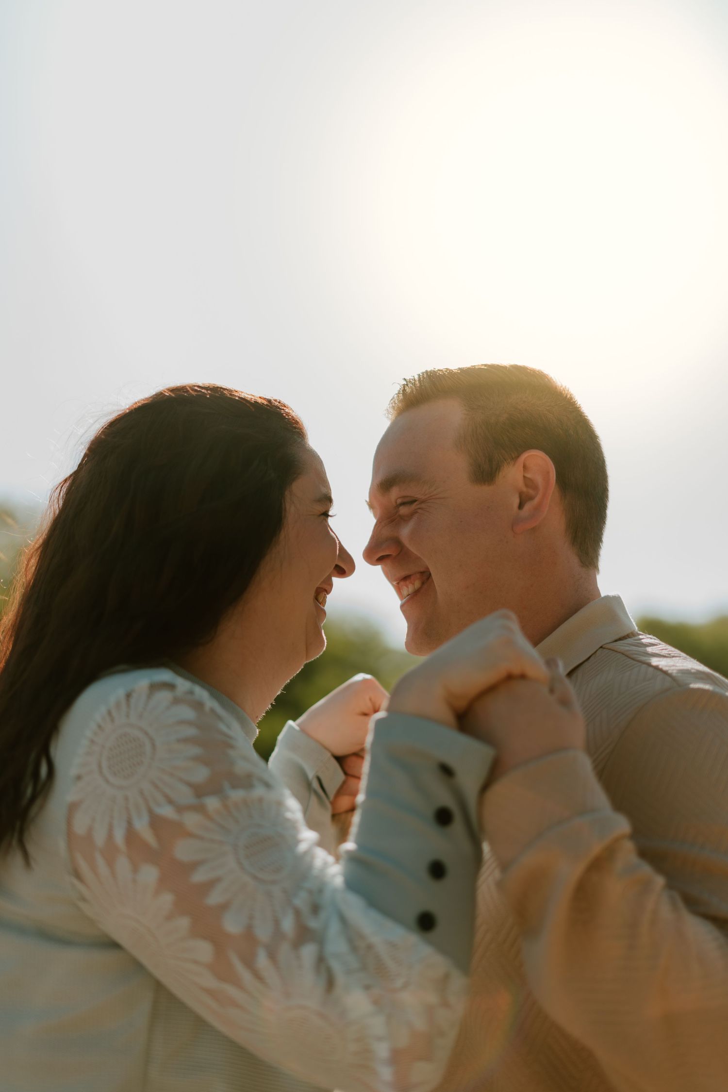 A joyful couple shares a romantic moment outdoors, smiling at each other in warm golden sunlight.