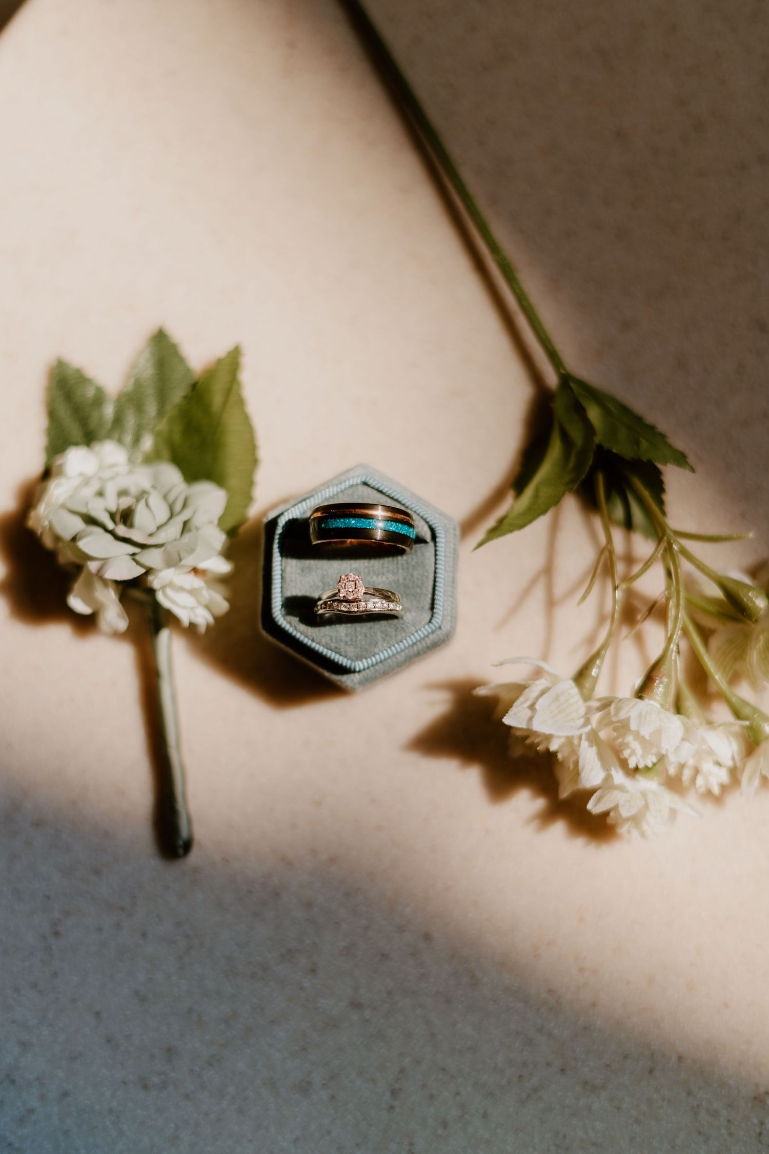 Two wedding rings displayed in a hexagonal velvet box surrounded by delicate white flowers.