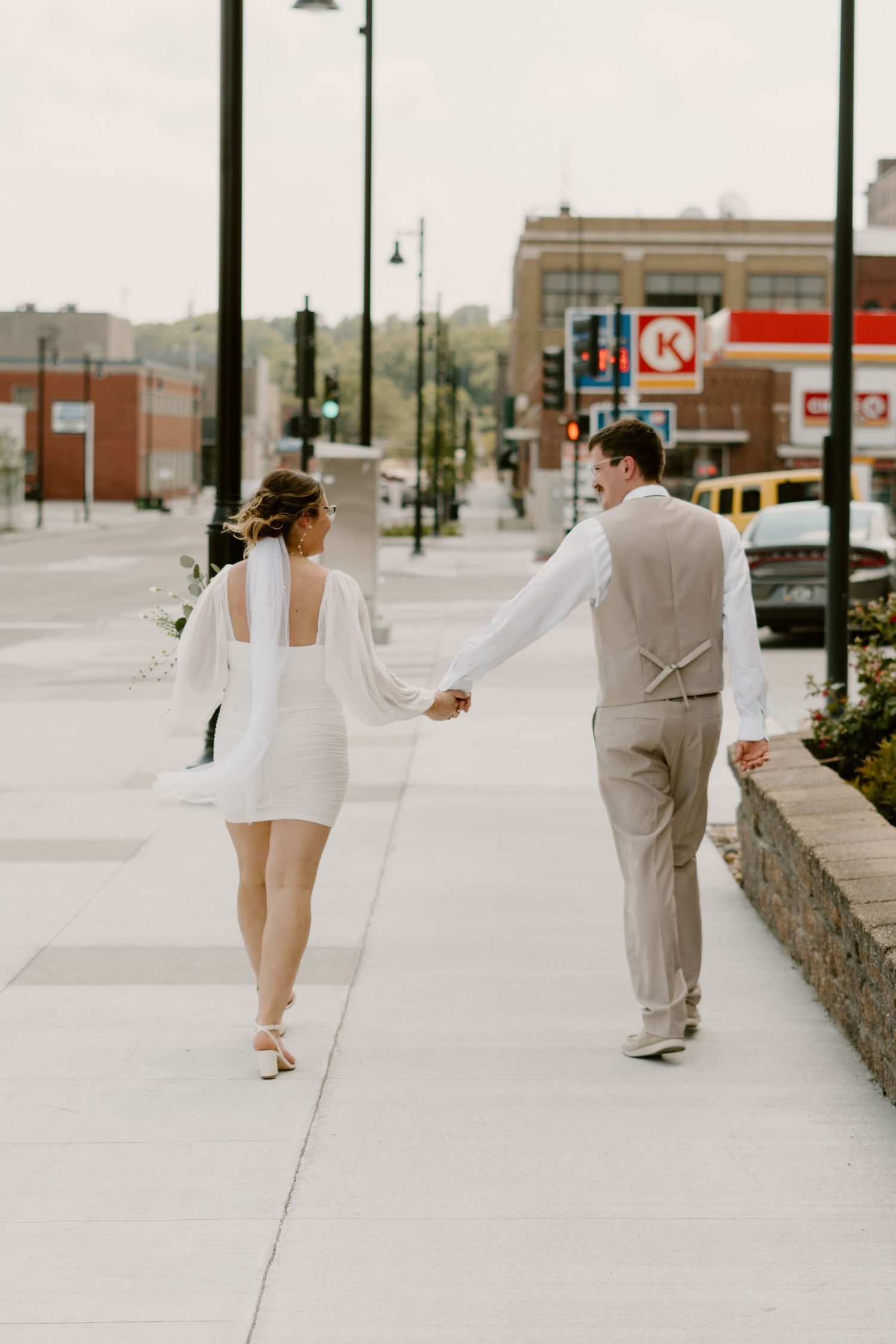 Bride and groom walk hand-in-hand down a city sidewalk after their elopment.