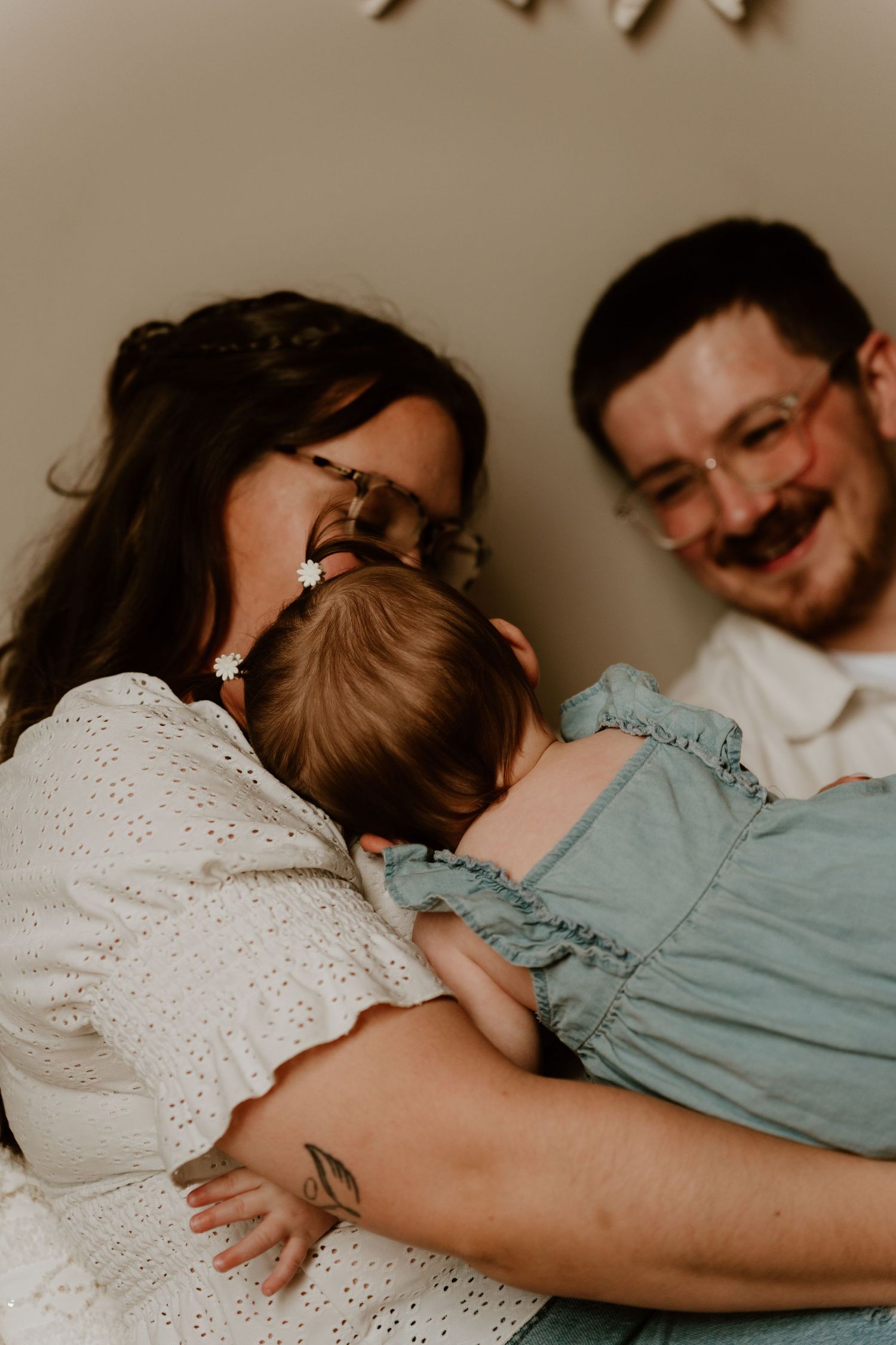 Happy parents smiling while holding their baby dressed in a teal outfit during a warm family photo session.