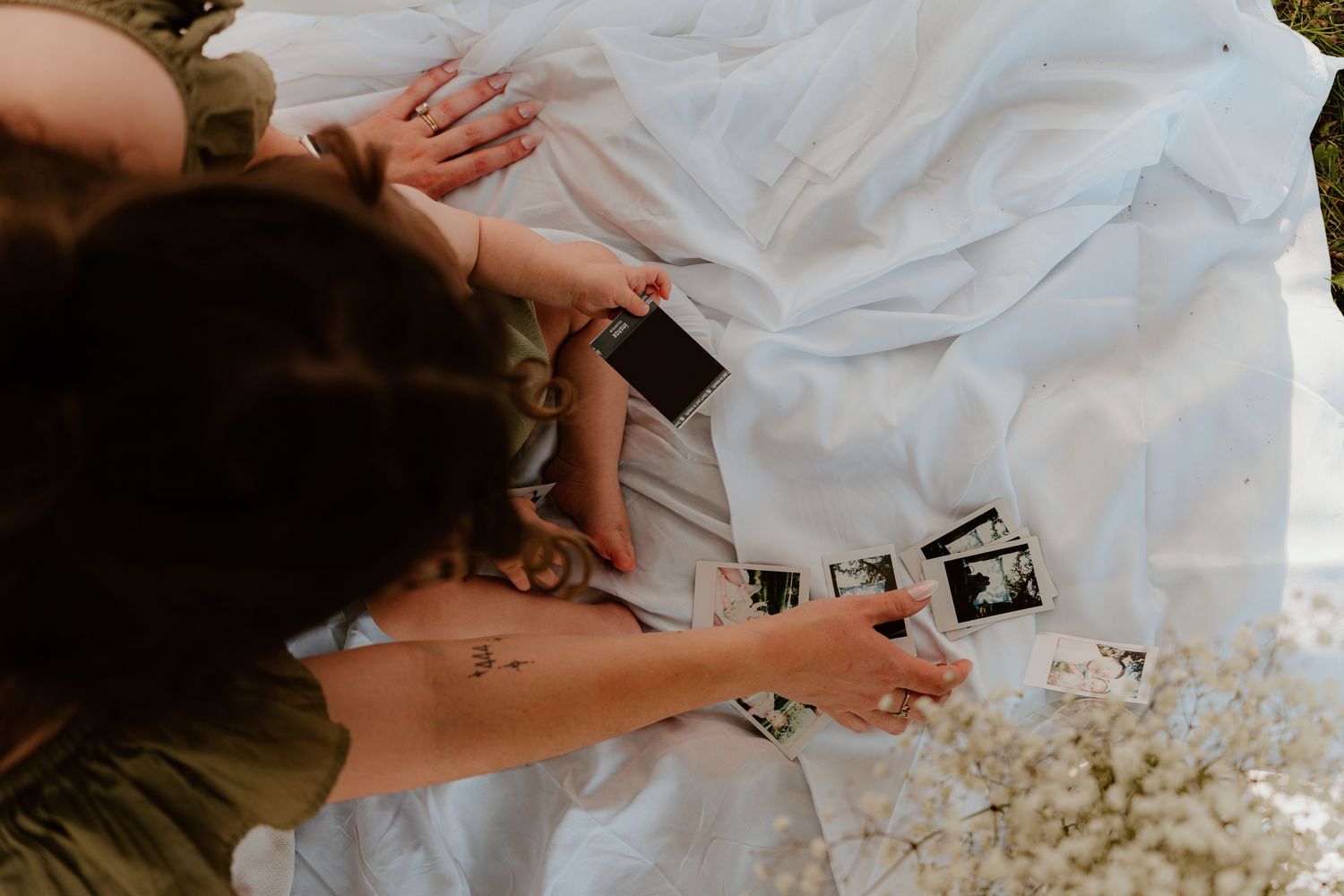 Overhead view of a woman looking at ultrasound photos on a white blanket with baby feet and flowers nearby.