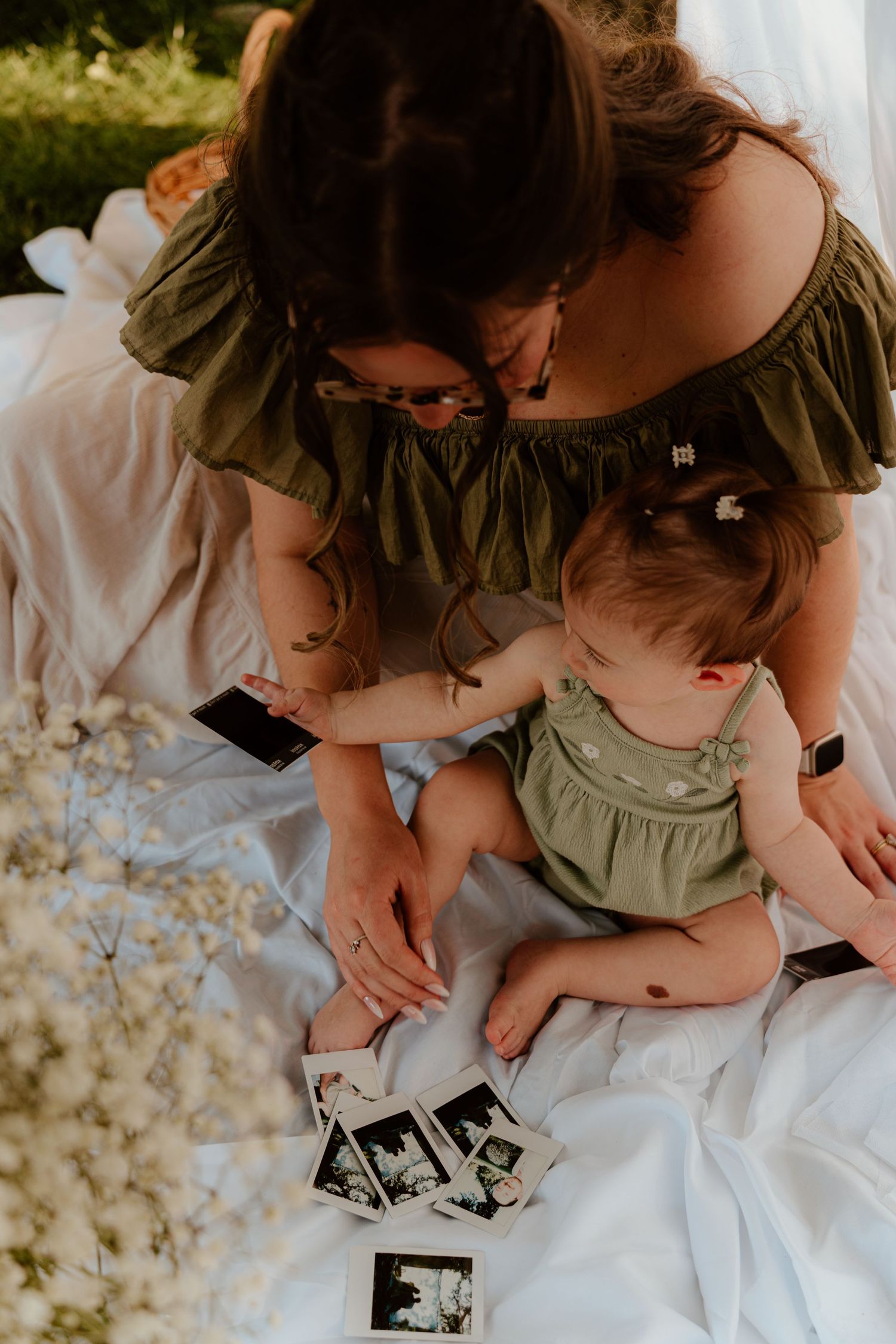 Mother and baby in matching green outfits looking at ultrasound photos on a white blanket outdoors.