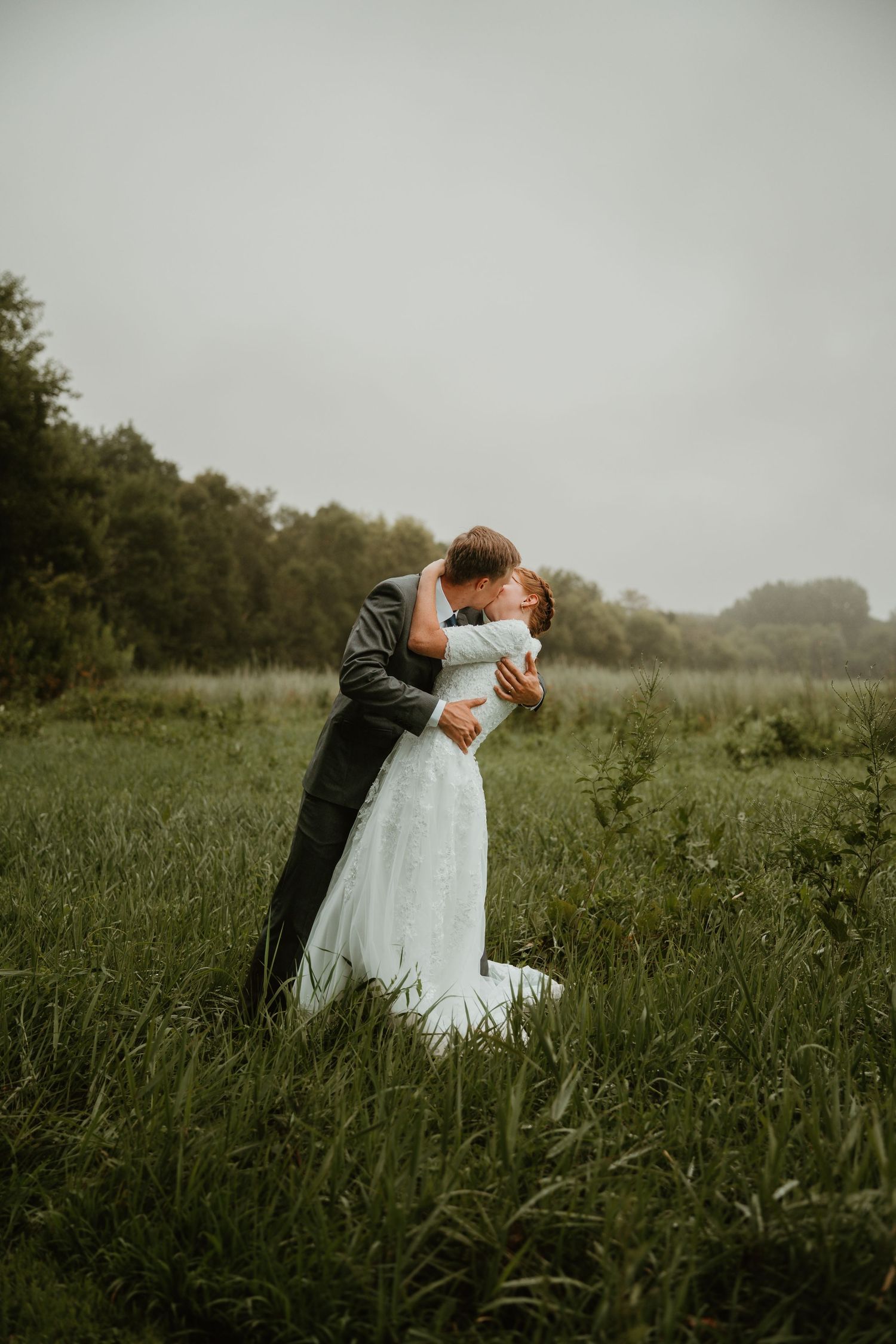 A bride and groom share a romantic kiss in a lush green field on their wedding day.