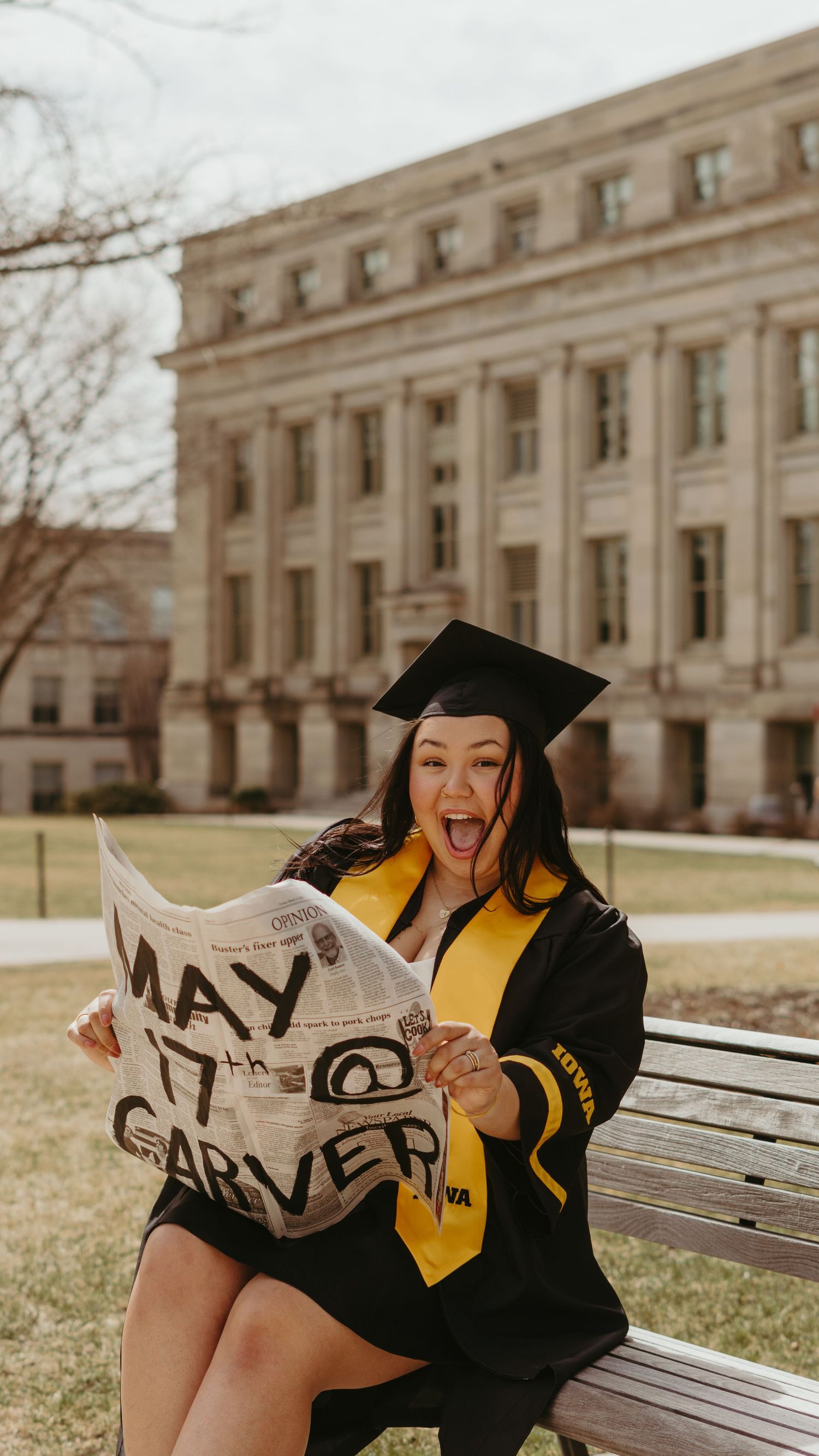 Excited University of Iowa graduate reacts to a newspaper showing her date of graduation at Carver.