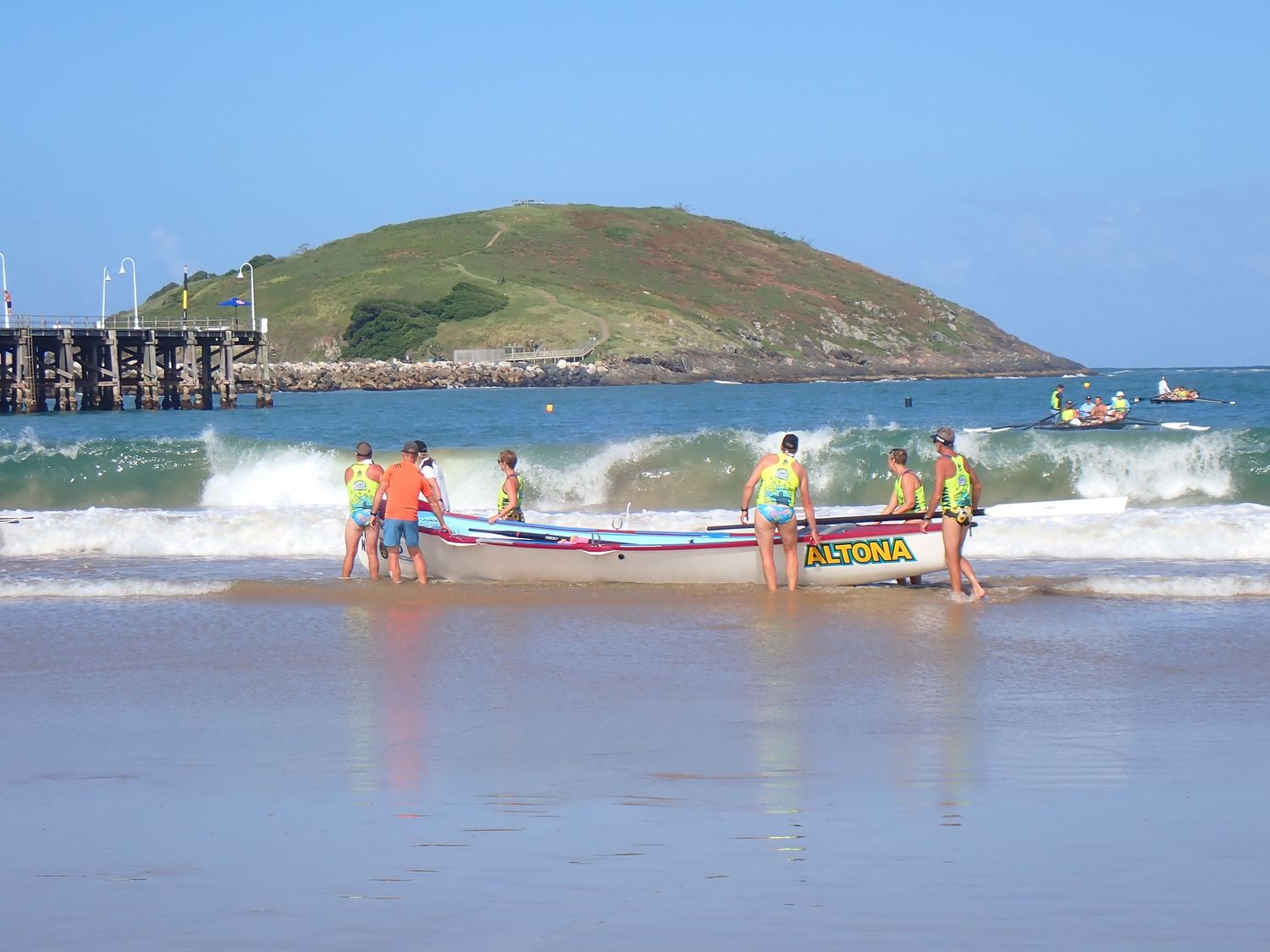 A sequence of surfing rescue boats navigating rough ocean waves near a coastal shoreline.