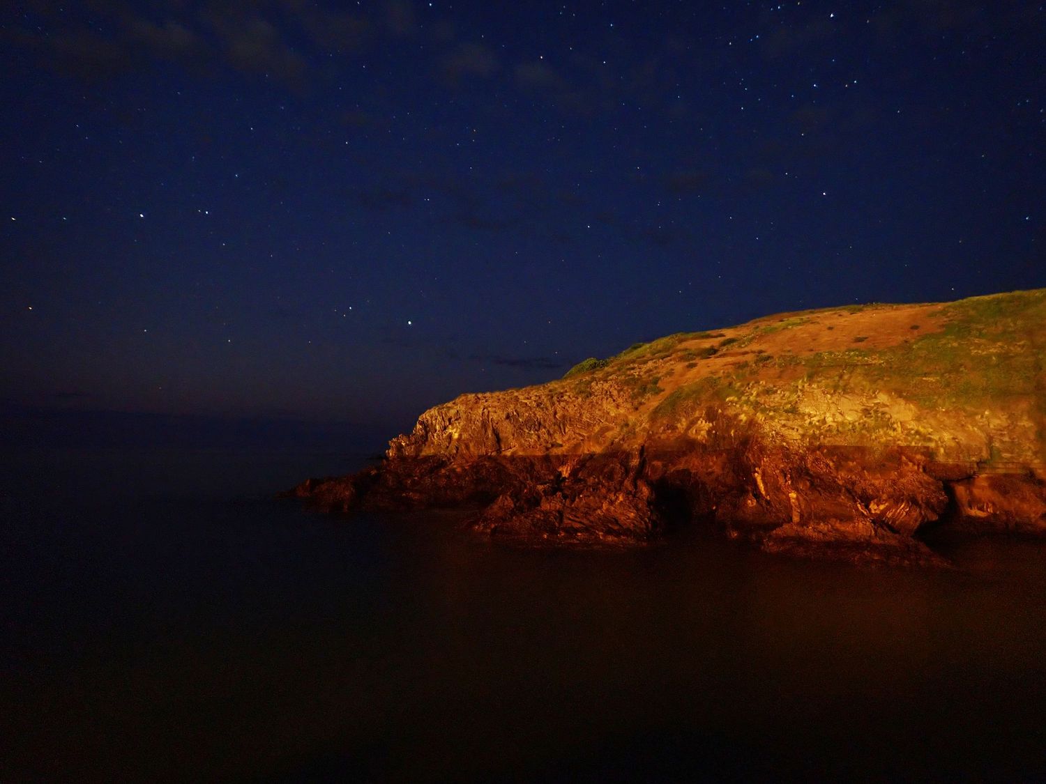 Mutton Bird Island, Coffs Harbour, illuminated by golden sunlight against a dark starry night sky.