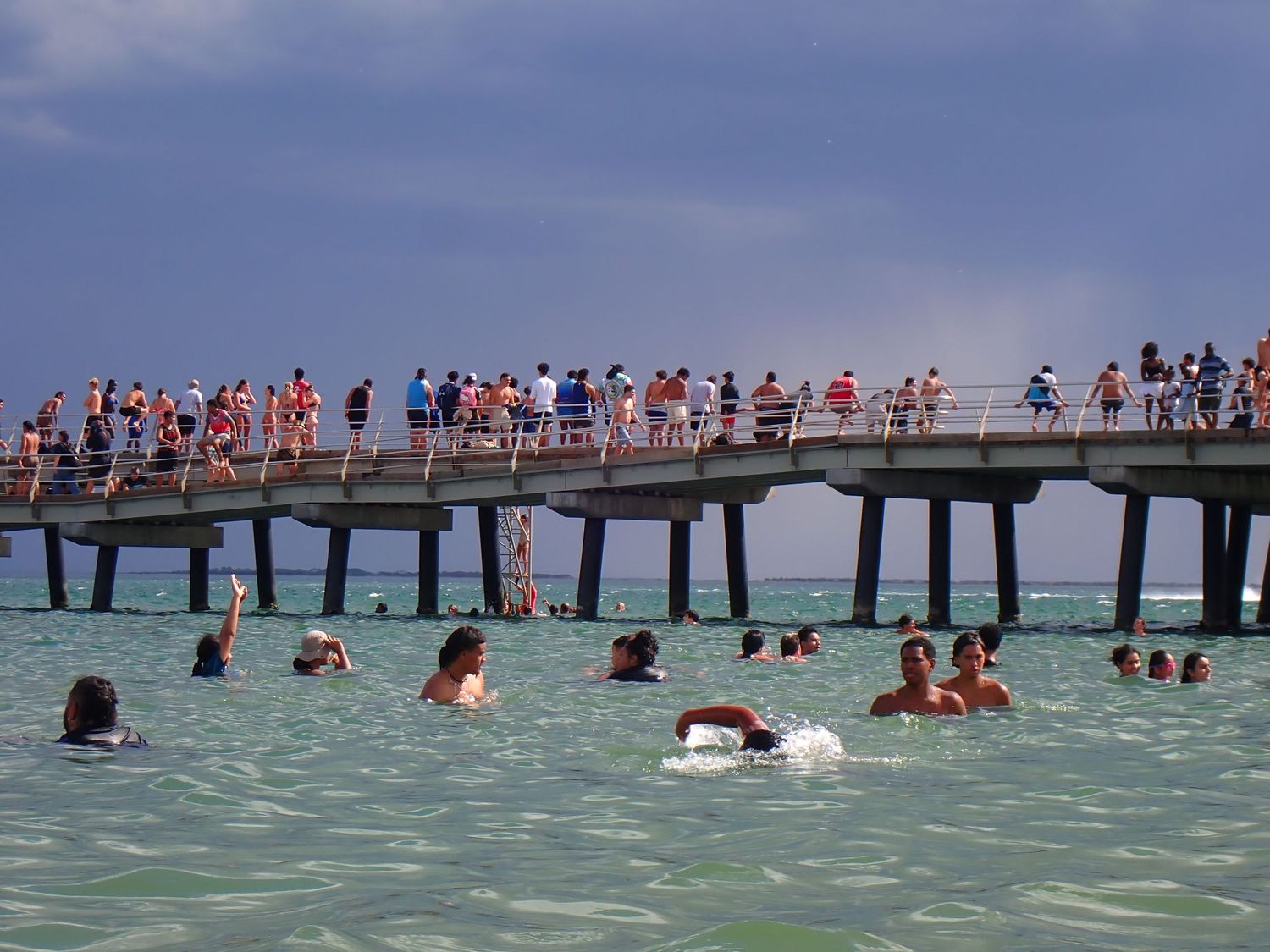 Beachgoers enjoy summer day on wooden pier stretching over turquoise ocean waters. Altona Pier