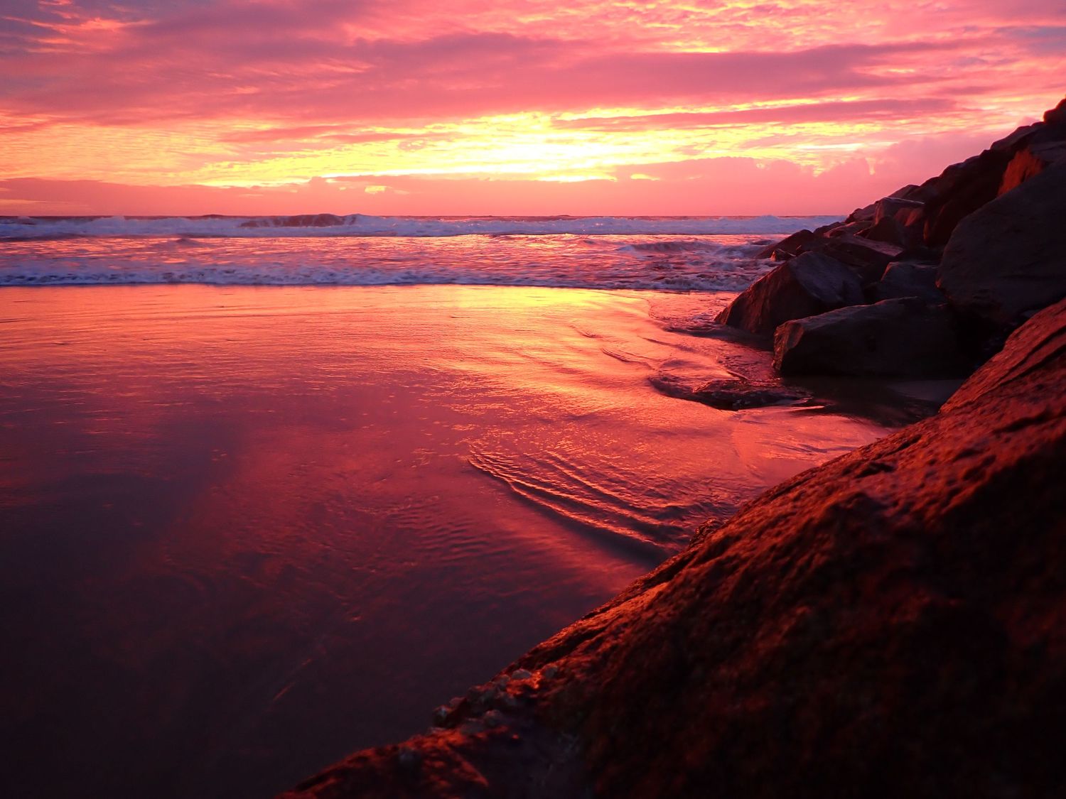 Dramatic pink and orange sunset sky reflects over calm coastal waters with silhouetted cliffs. Coffs North Wall at Sunrise.