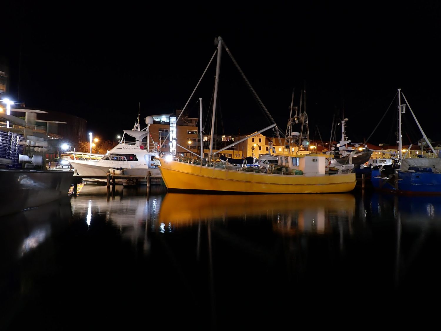 Nighttime marina with boats and buildings illuminated against dark waters. Hobart Marina.