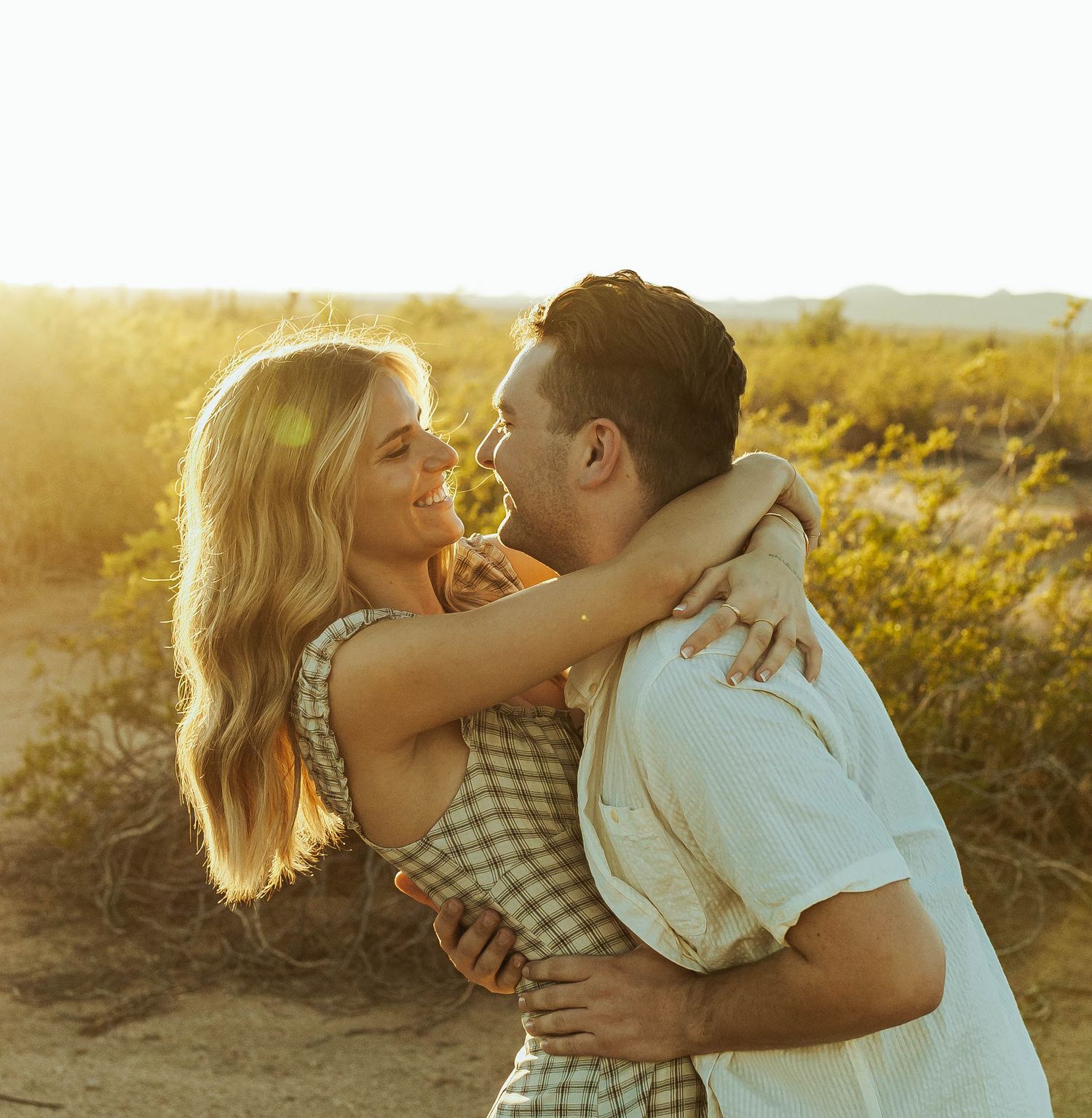 A couple embraces during a sunset photoshoot in a desert landscape.