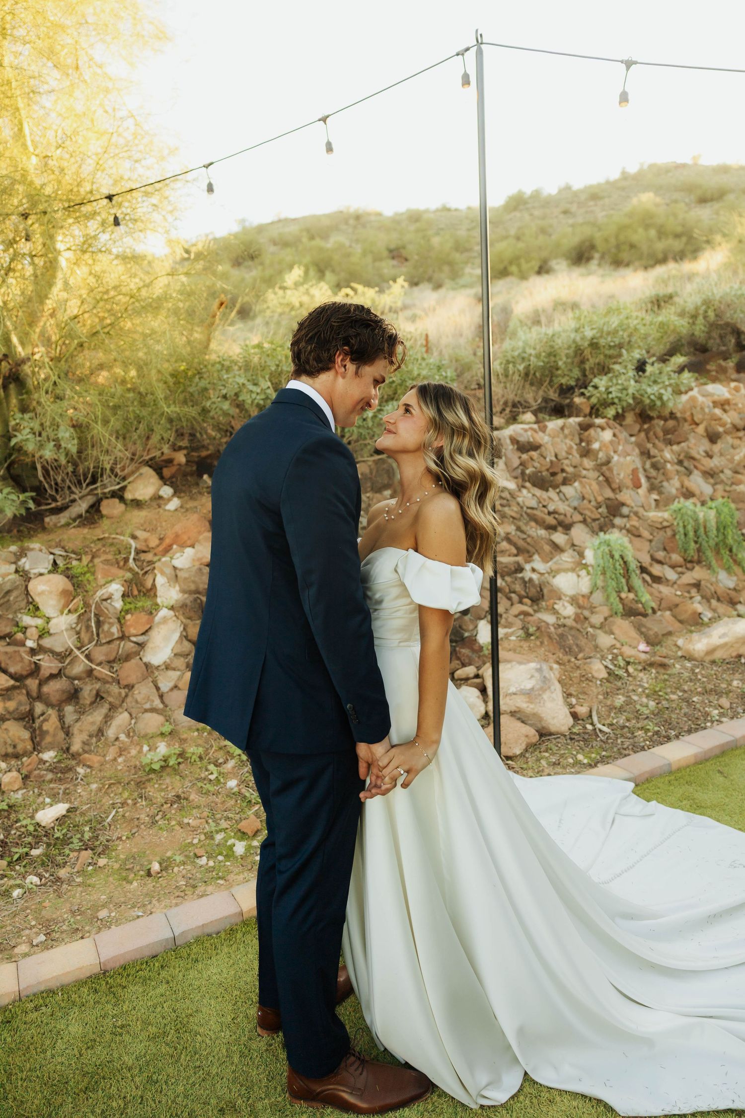 A couple shares a romantic moment under string lights at their outdoor desert wedding.