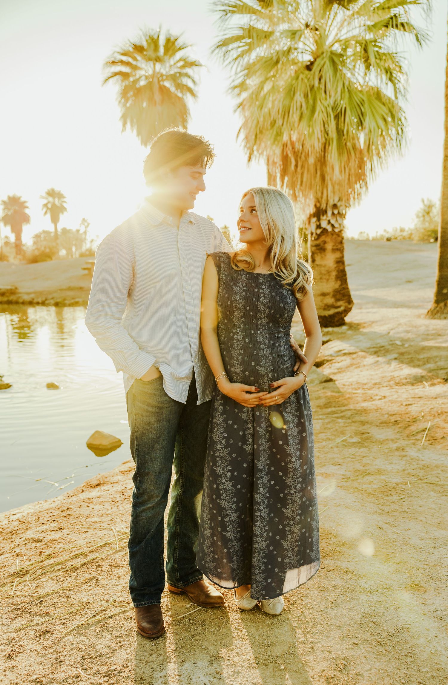 A couple stands together near palm trees at sunset in a romantic desert photoshoot.