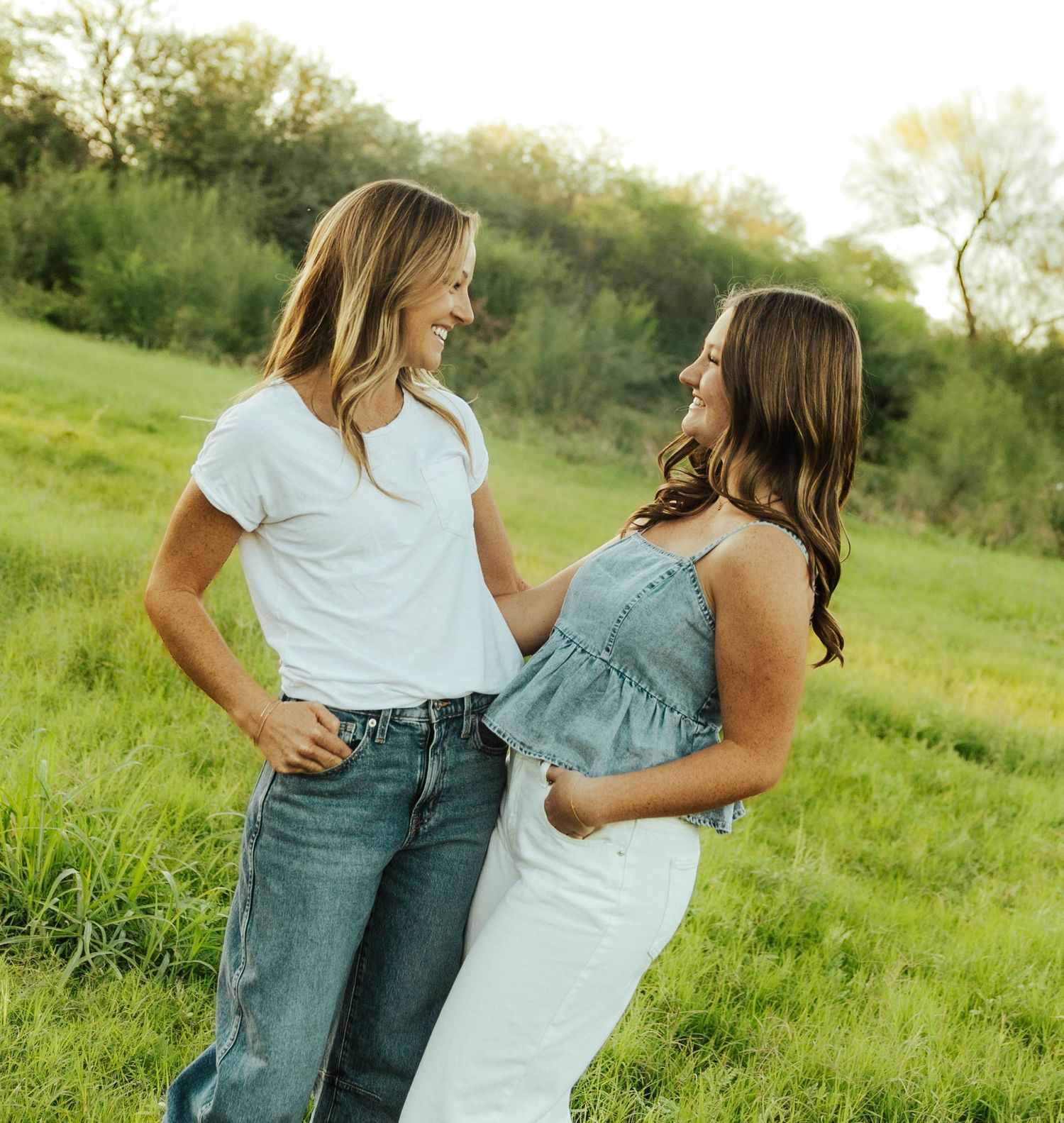 A couple embraces while standing in a sunny green meadow wearing coordinating blue and white outfits.