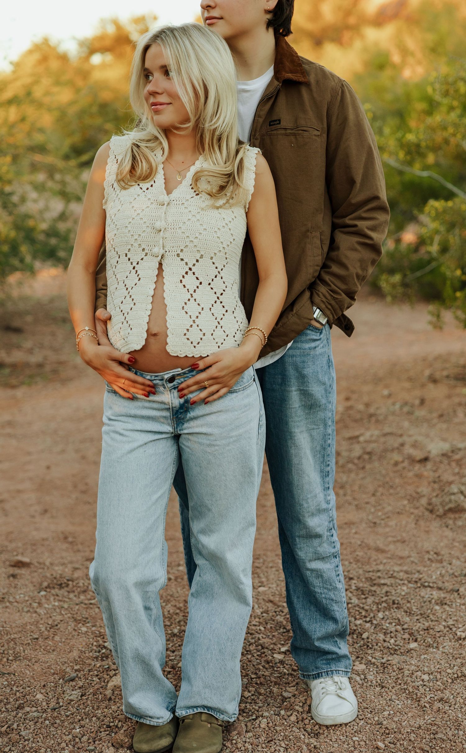 Couple in casual denim and white crochet top embracing during golden hour outdoors.