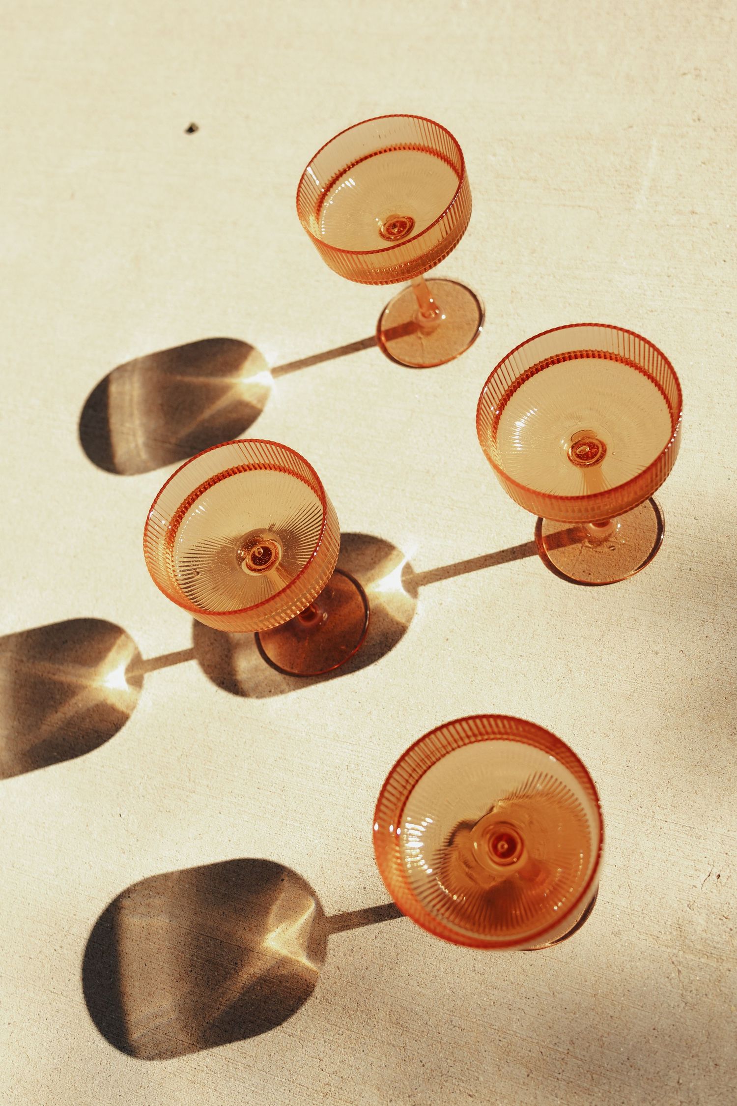 Pink champagne glasses casting dramatic shadows on a light surface in an artistic arrangement.