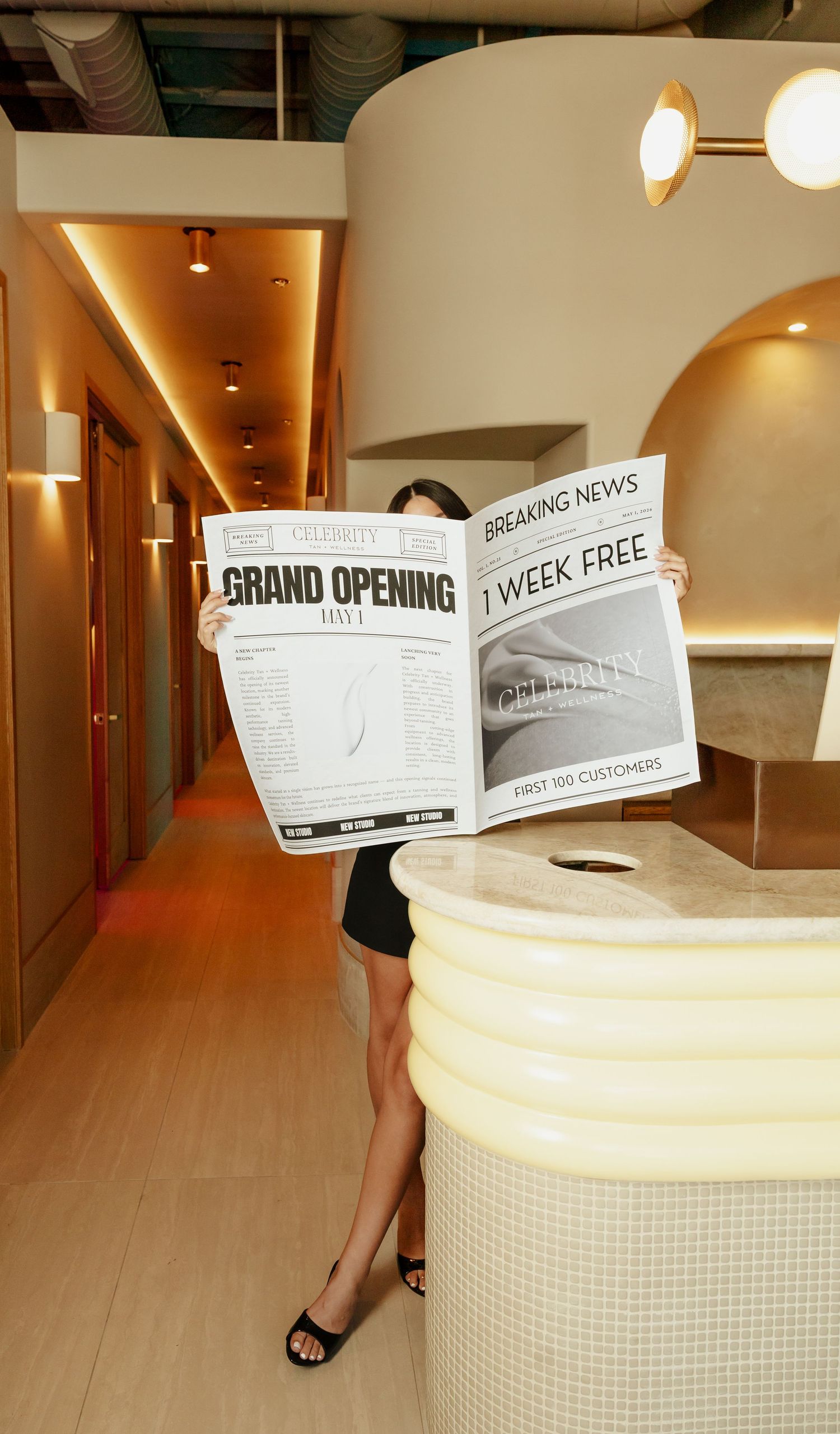 Person holding a newspaper announcing a grand opening with 1 week free offer for first 100 customers in a modern interior.