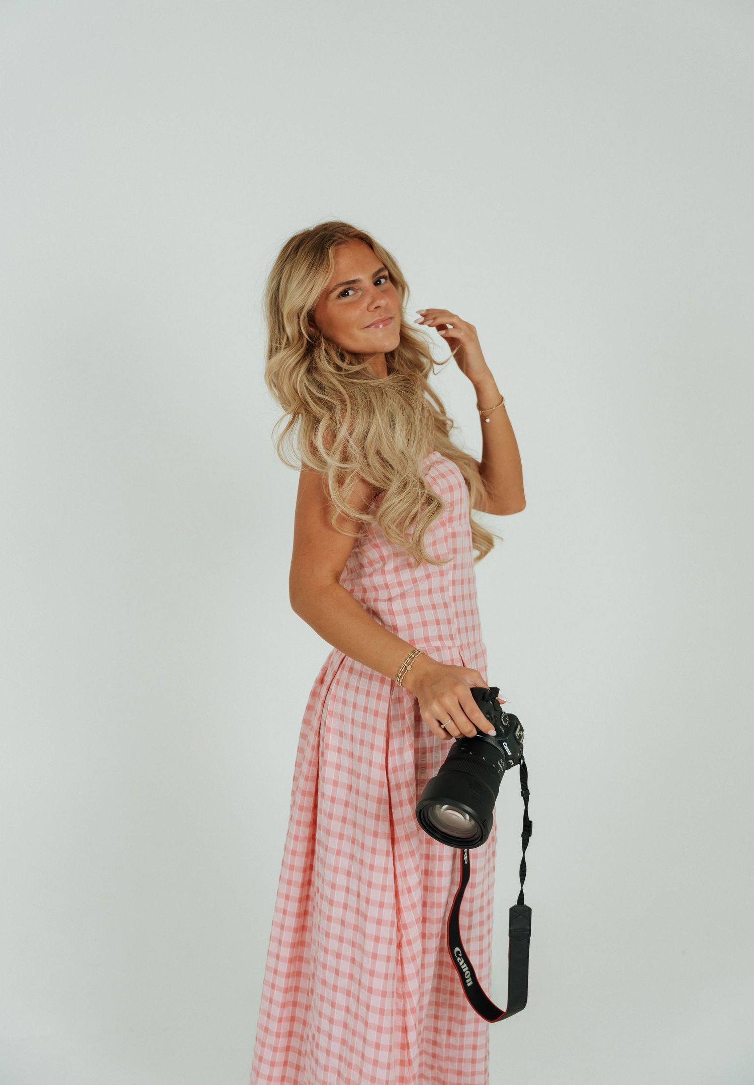A series of four photos showing someone in a pink gingham dress posing with a black camera against a white background.