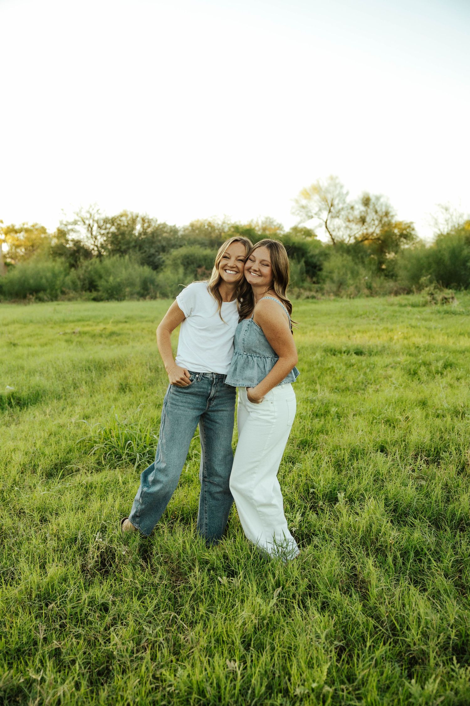 Two people in casual outfits share a playful moment together in a sunlit green meadow during golden hour.