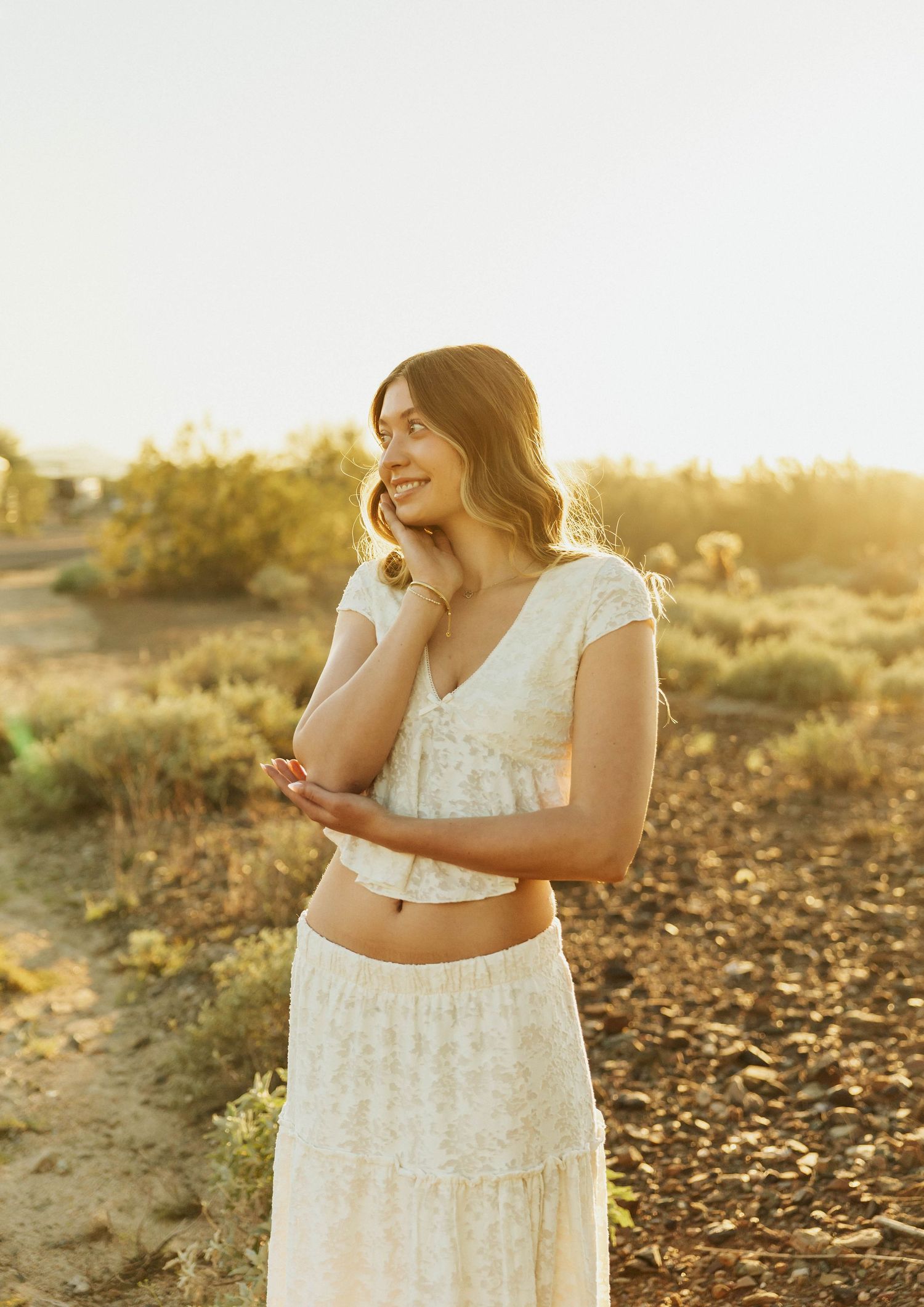 Woman in white dress poses elegantly during desert sunset.