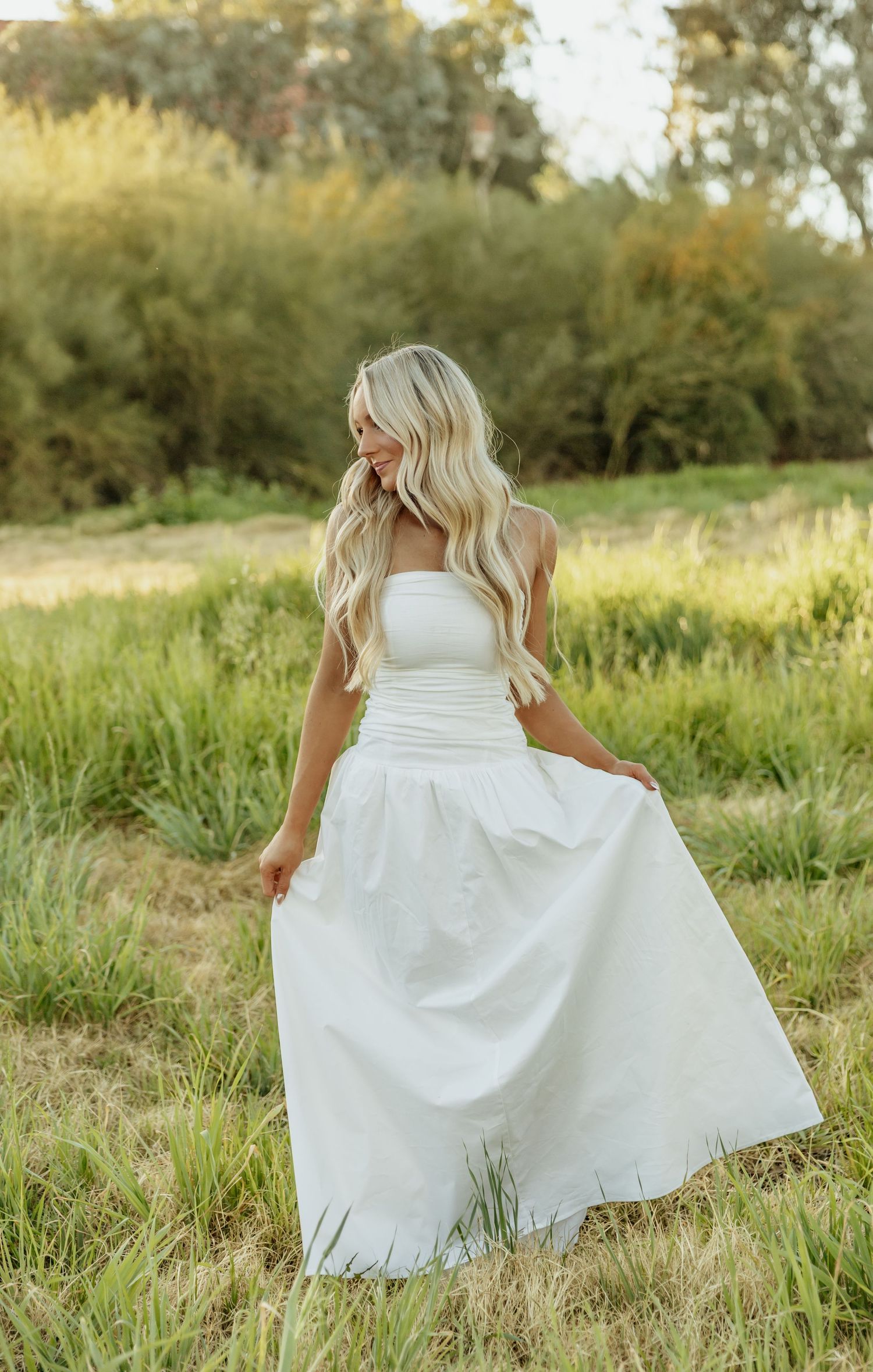 Elegant white wedding dress with strapless design photographed in golden field at sunset.